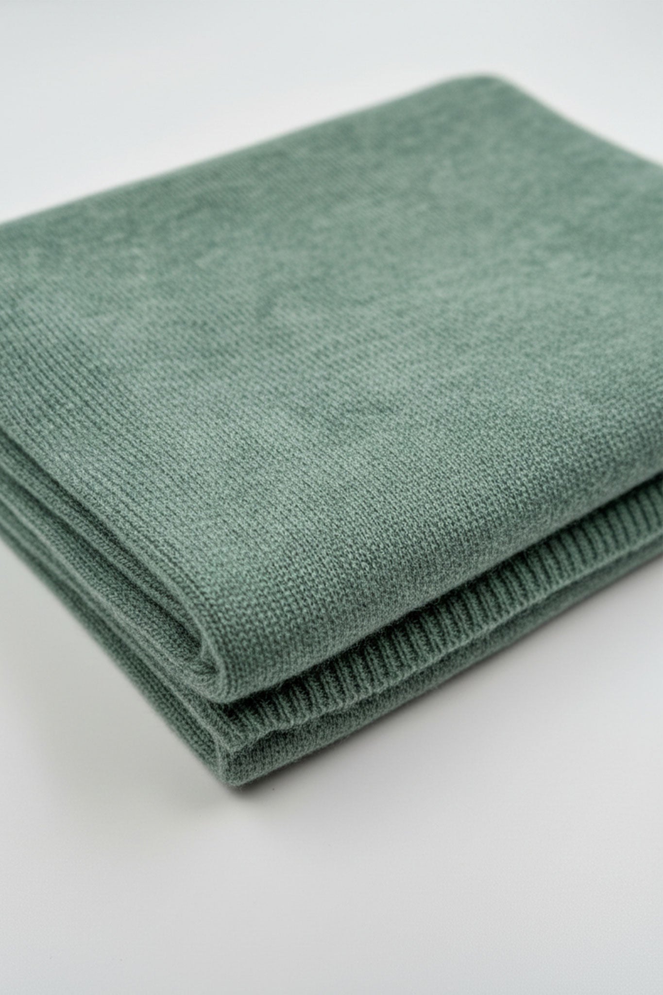 Détail de l'écharpe en cachemire vert sauge, soulignant sa texture soyeuse, un accessoire élégant pour les soirées chics.