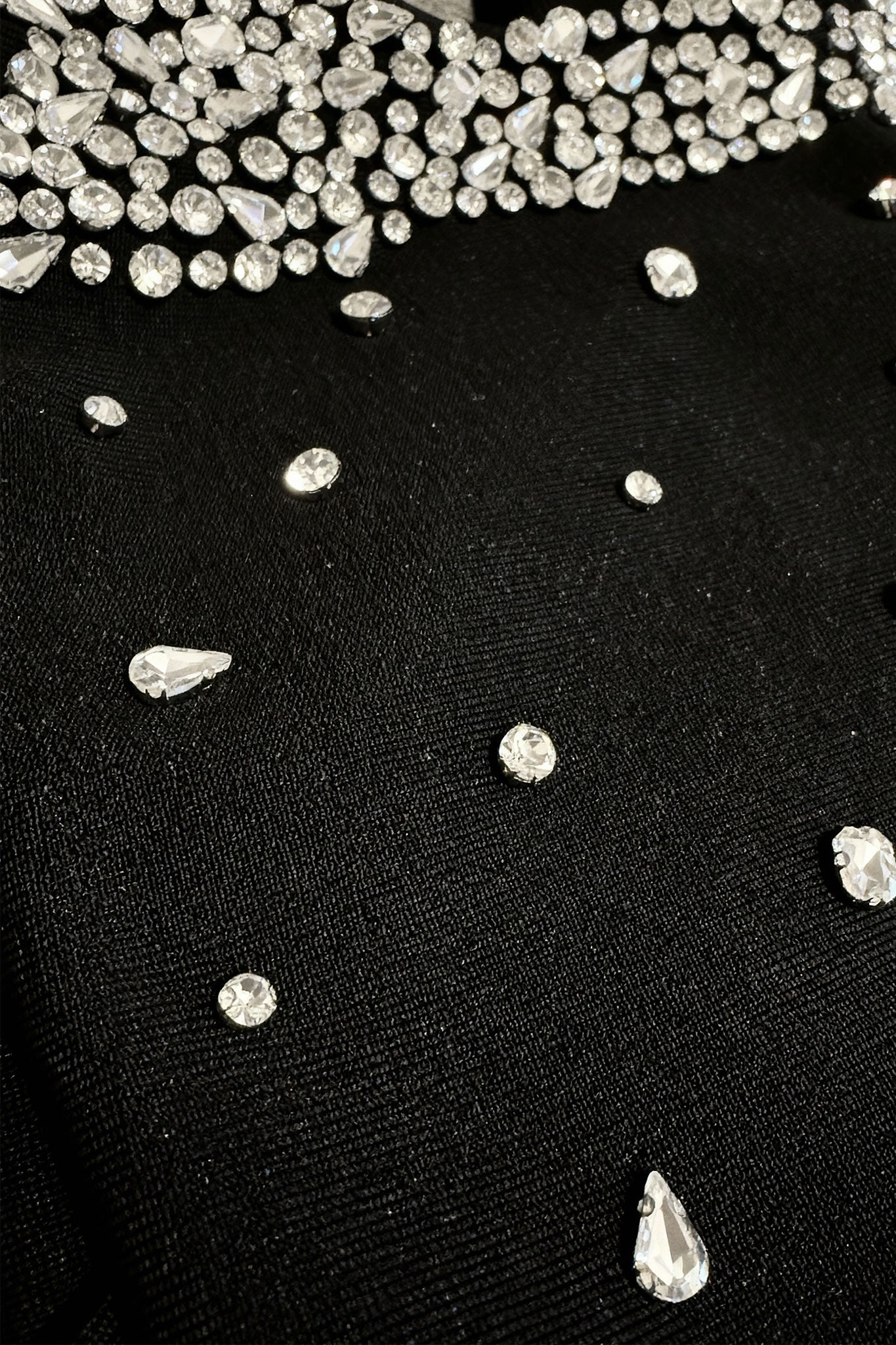 Détail captivant d'une robe noire courte mettant en avant les perles éclatantes et les nœuds raffinés aux épaules.