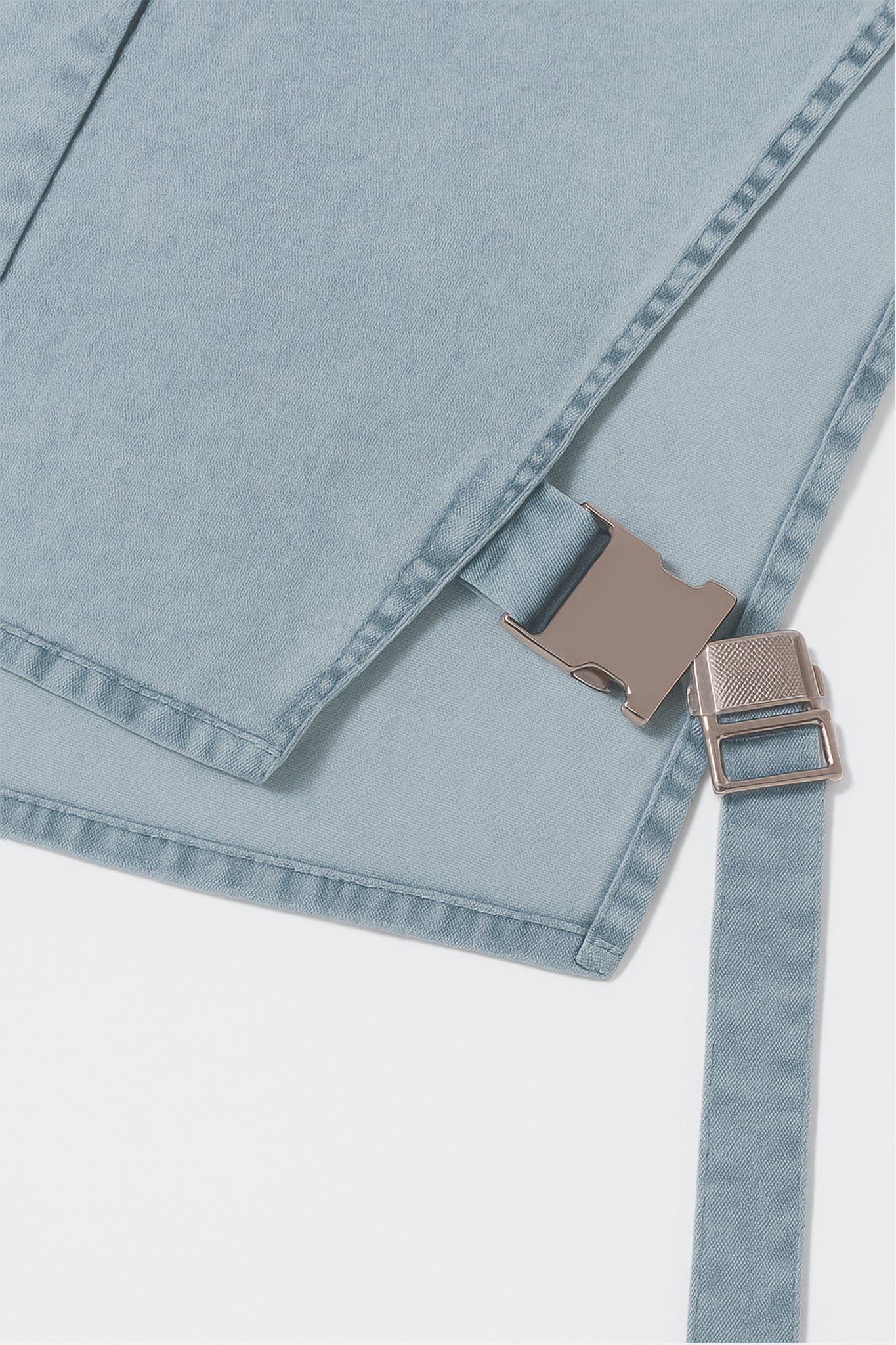 Détail du top en denim bleu structuré, mettant en avant une boucle métallique, pour une touche élégante au quotidien.
