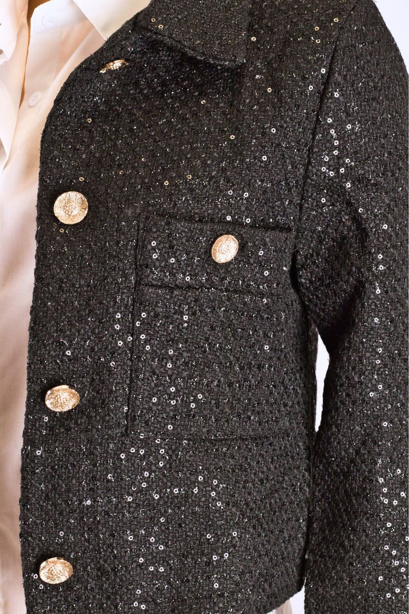 Détail raffiné de la veste courte en tweed noir avec sequins, parfaite pour une allure chic lors d'une soirée élégante.