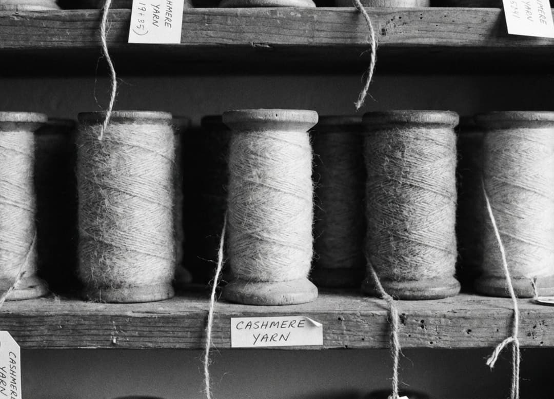 Bobines de fil de cachemire alignées sur une étagère en bois, saisies en macro noir et blanc au grain marqué et aux ombres douces.