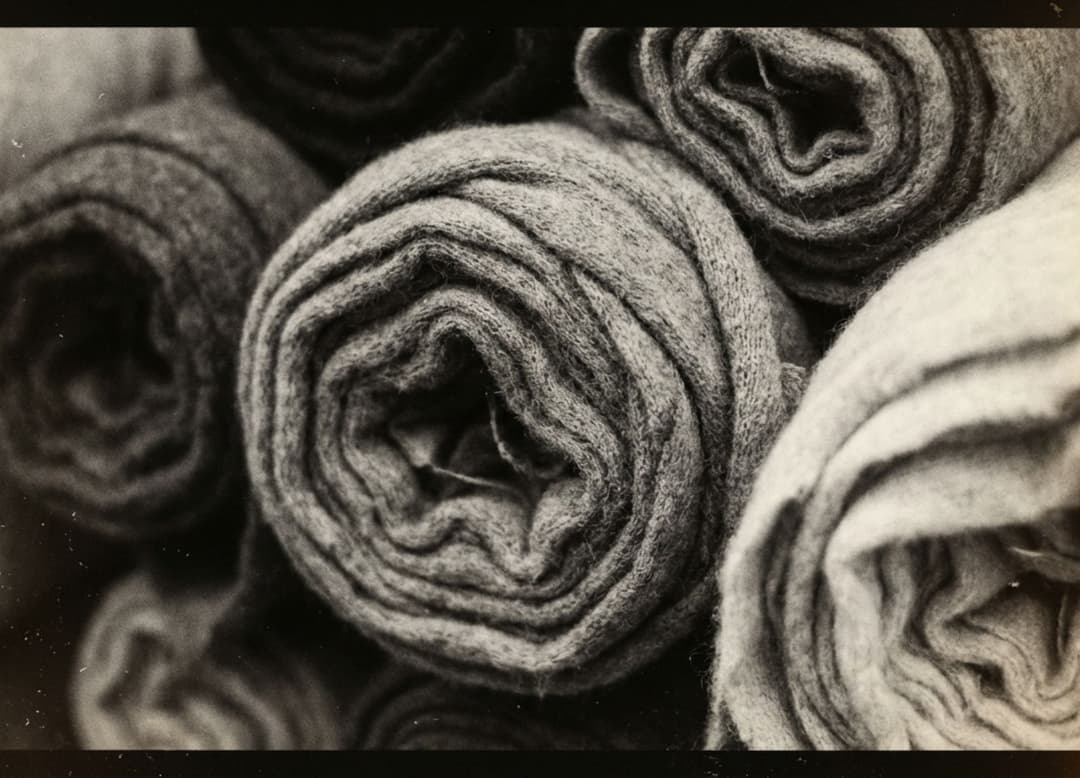 Rouleaux de tissu en cachemire serrés les uns contre les autres, montrés en macro noir et blanc avec texture laineuse et grain visible.