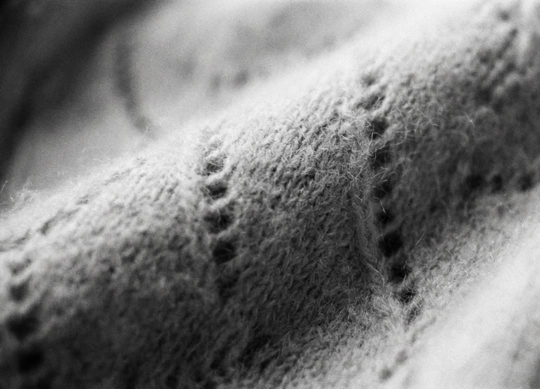 Gros plan en noir et blanc sur un foulard en cachemire, révélant la texture douce et les mailles fines.