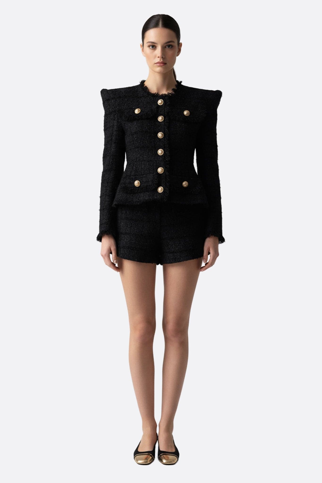 Elegante Damenjacke aus schwarzem Tweed, stilvoll getragen mit Shorts, perfekt für formelle Anlässe oder im Büro.