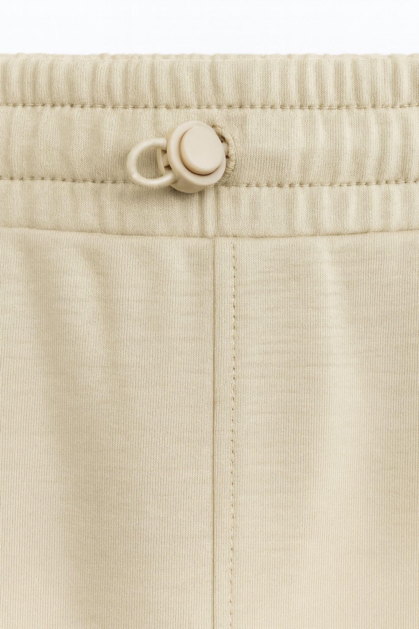 Perspective 3/4 du pantalon large beige en tissu technique, une pièce élégante à porter pour des occasions décontractées.