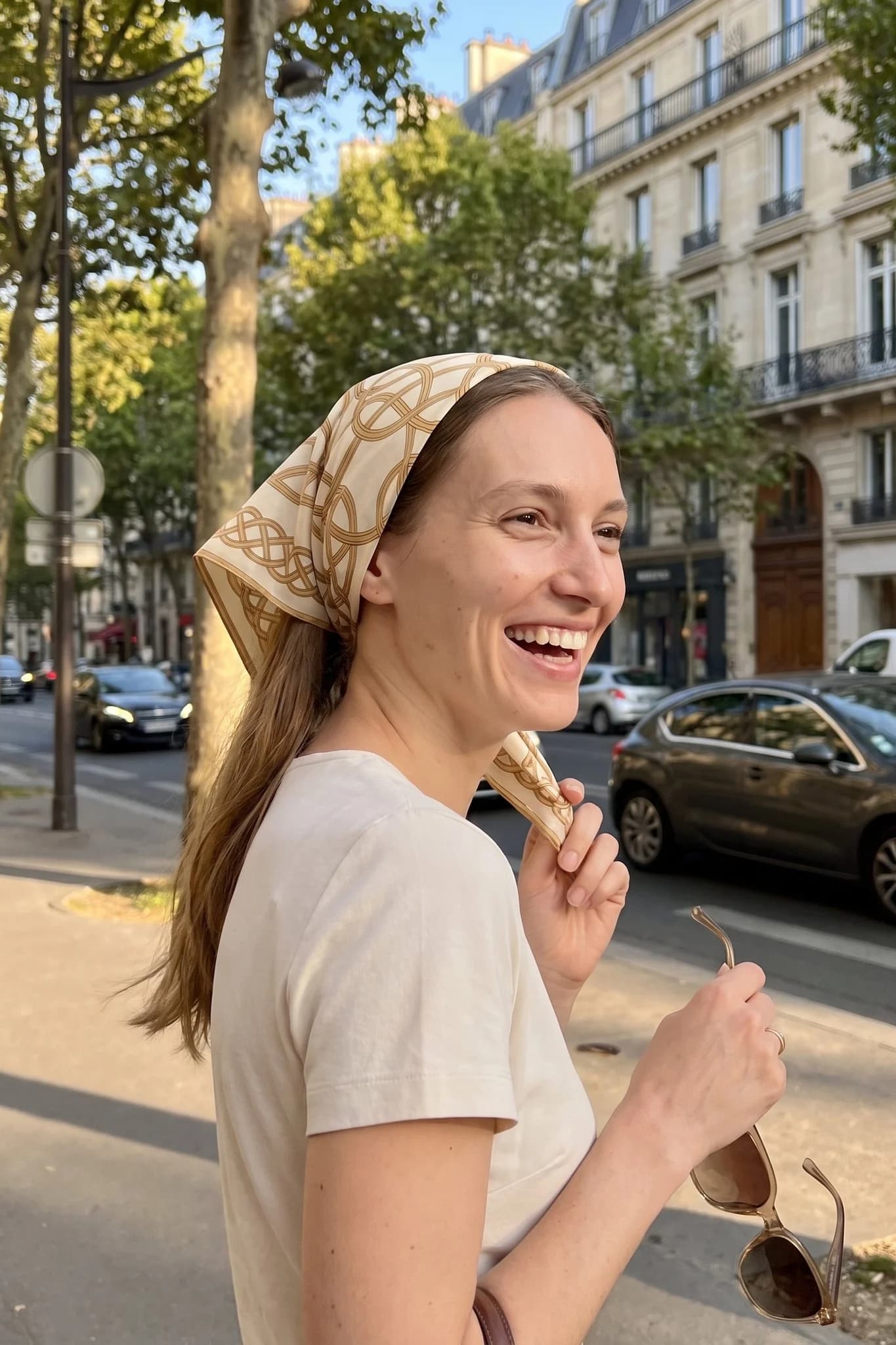 Woman wearing the silk scarf Entrelacs d'or as a bandana in her hair on a Paris street