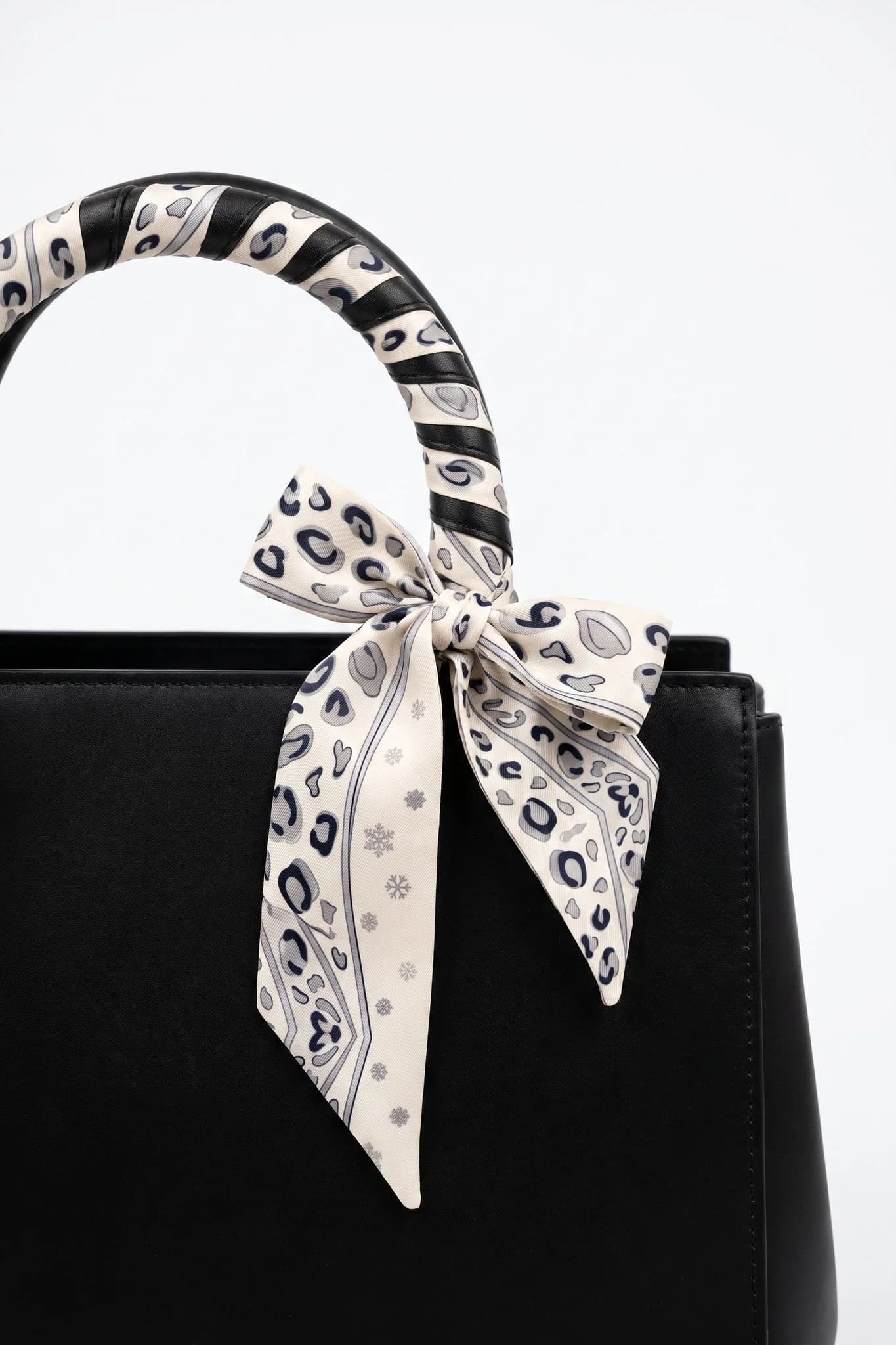 Snow leopard twilly wrapped and tied around the handle of a black leather bag