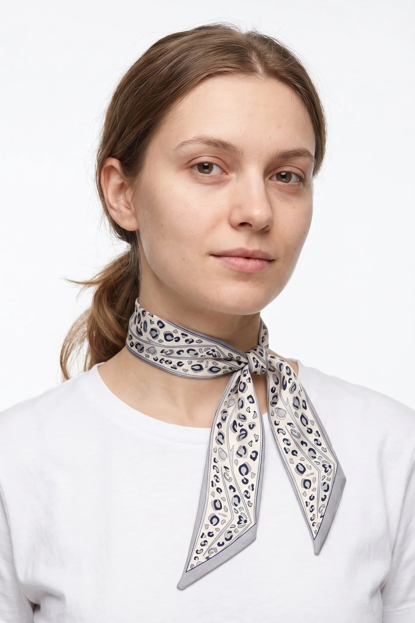 Snow leopard silk twilly tied as a thin necktie around a woman's neck, studio view