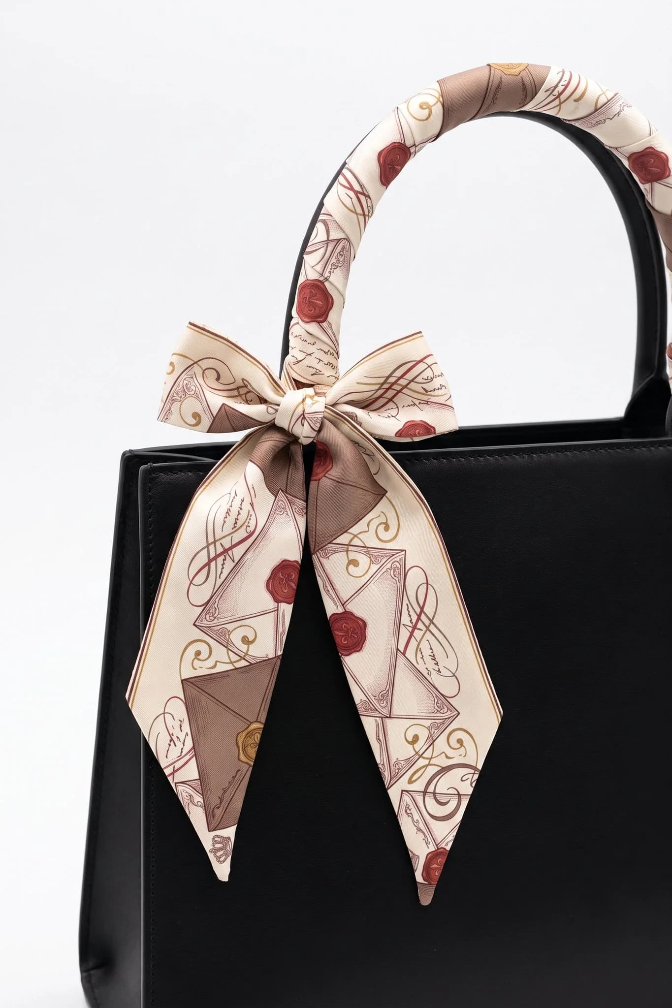 Twilly Lettres d'amour enroulé et noué autour de l'anse d'un sac en cuir noir