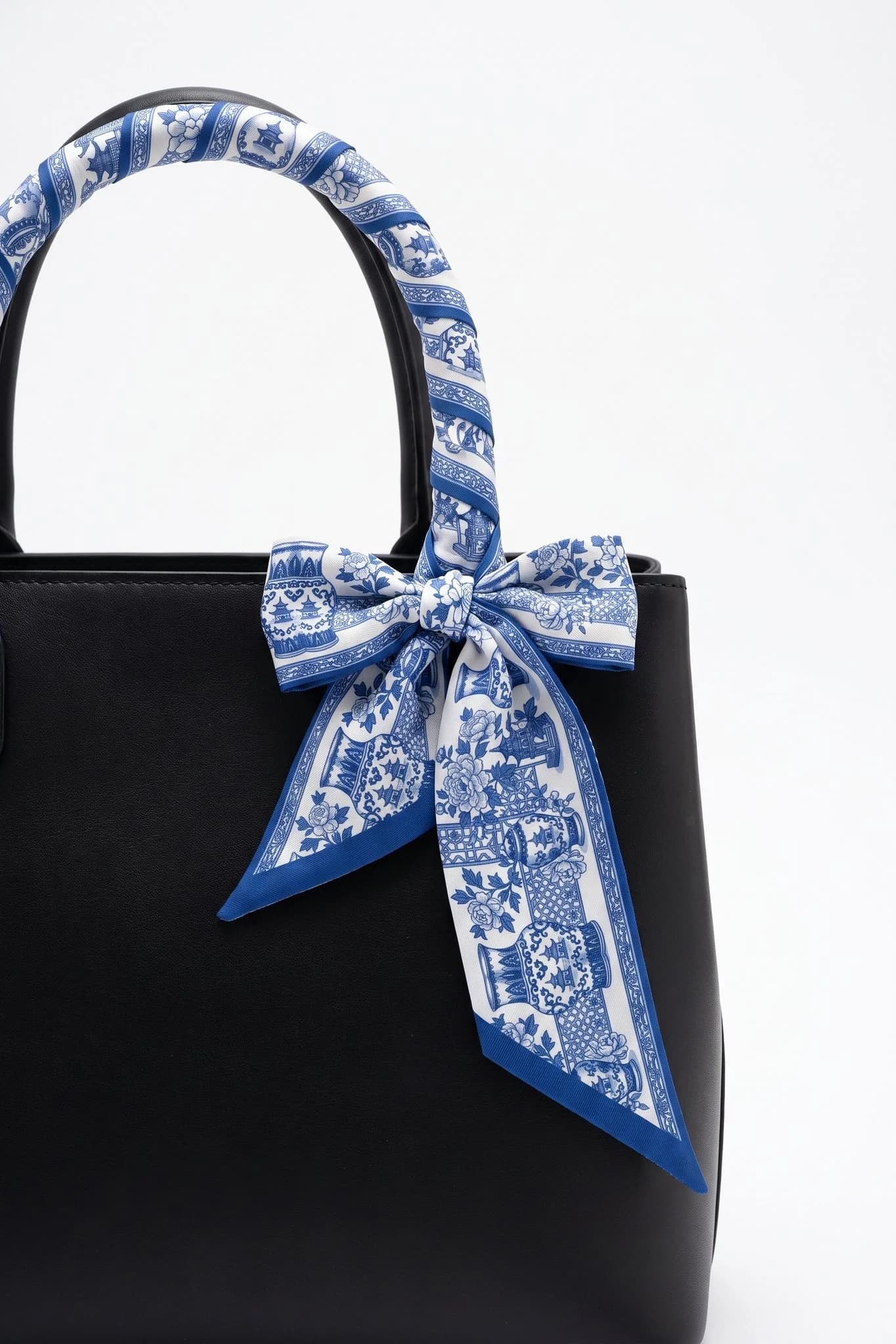 Twilly Porcellana blu arrotolato e annodato attorno al manico di una borsa in pelle nera
