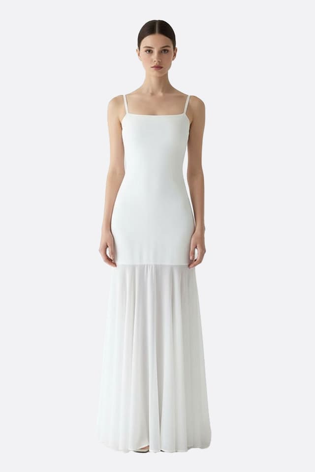 Abito lungo bianco con spalline delicate, con gonna trasparente e fluida, perfetto per una serata elegante.