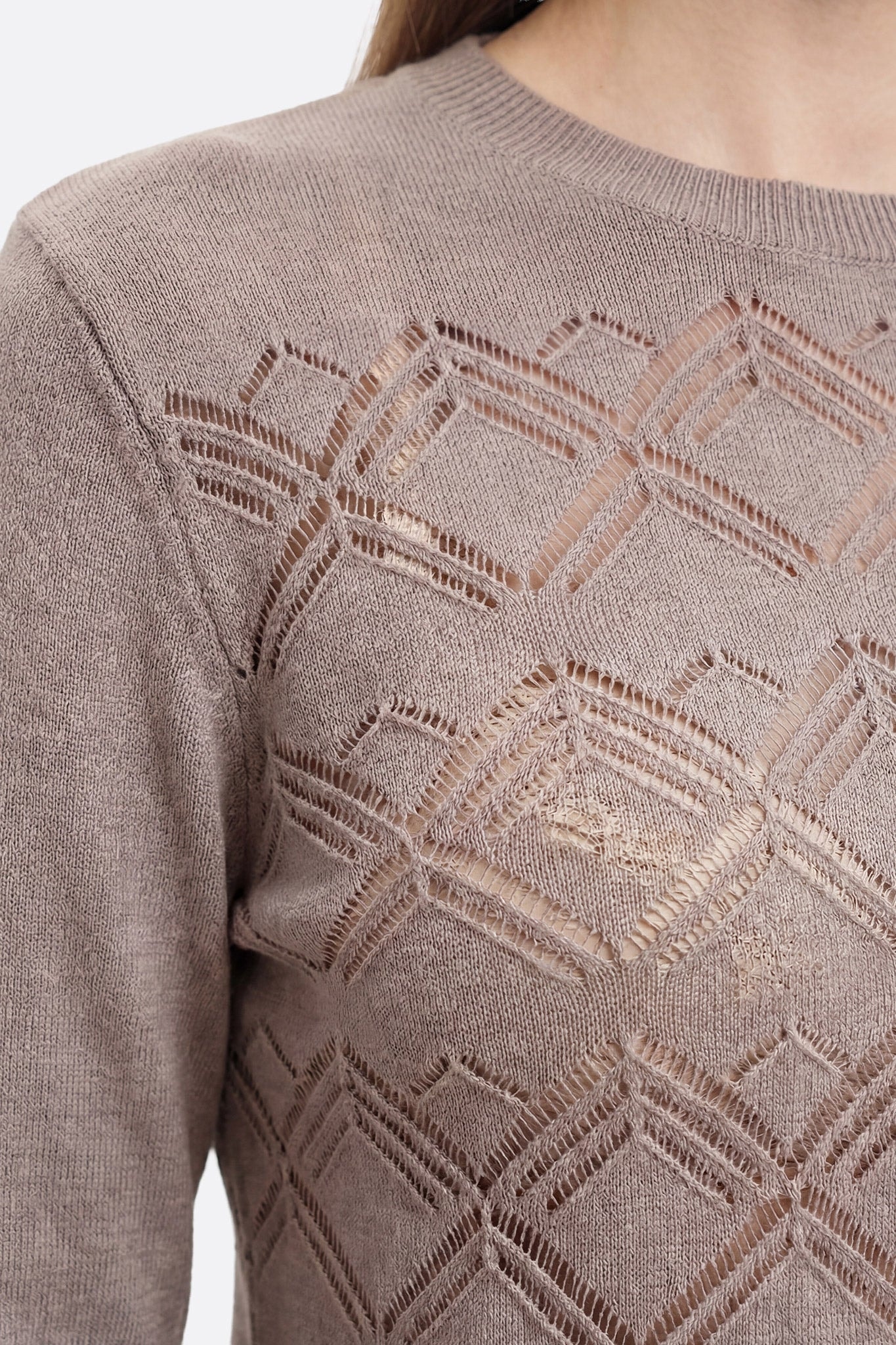 Primo piano sulla maglia traforata color taupe indossata, con motivo geometrico e texture