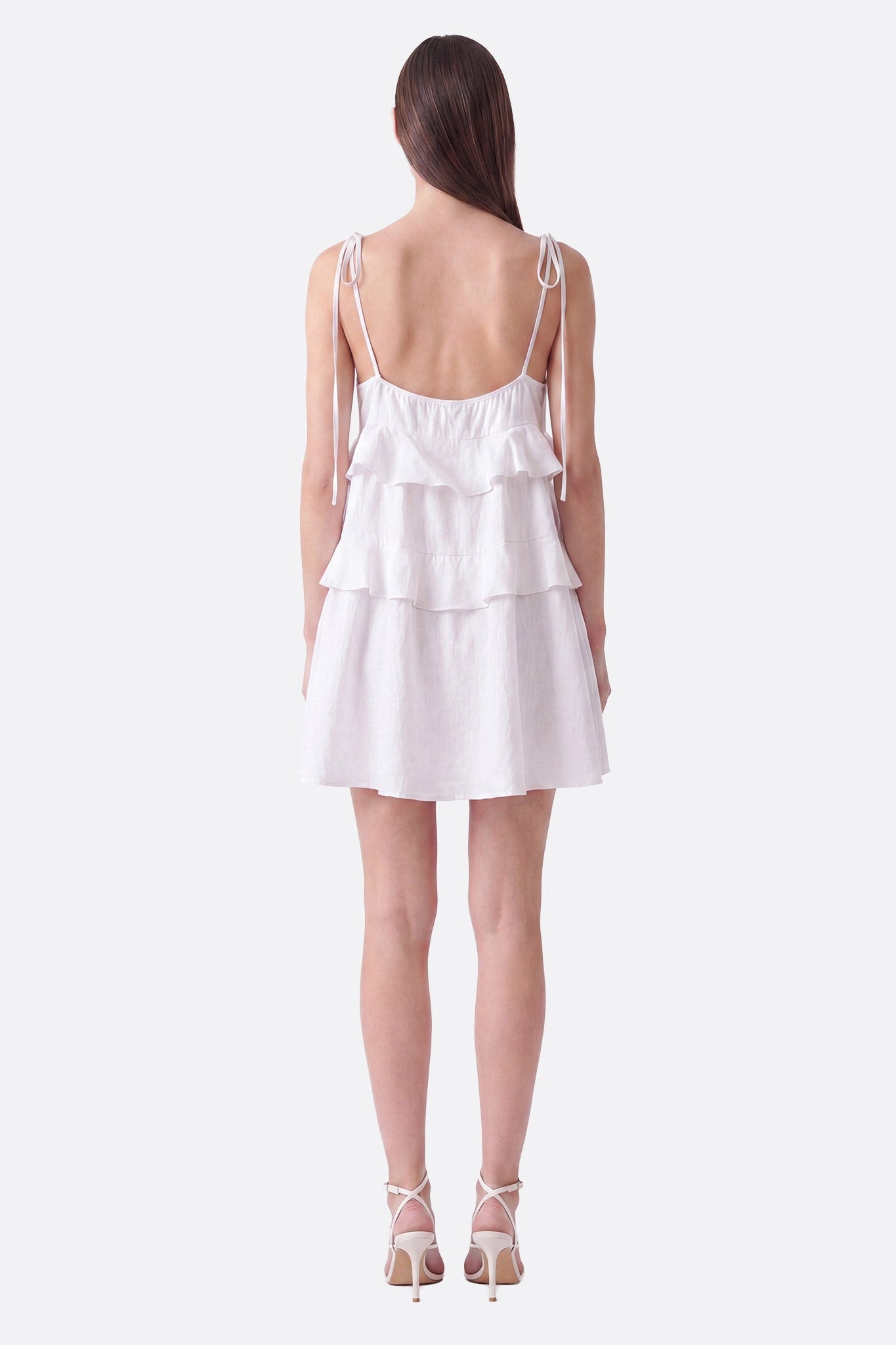 Short white dress with ruffles and tied straps worn from back, textured fabric visible
