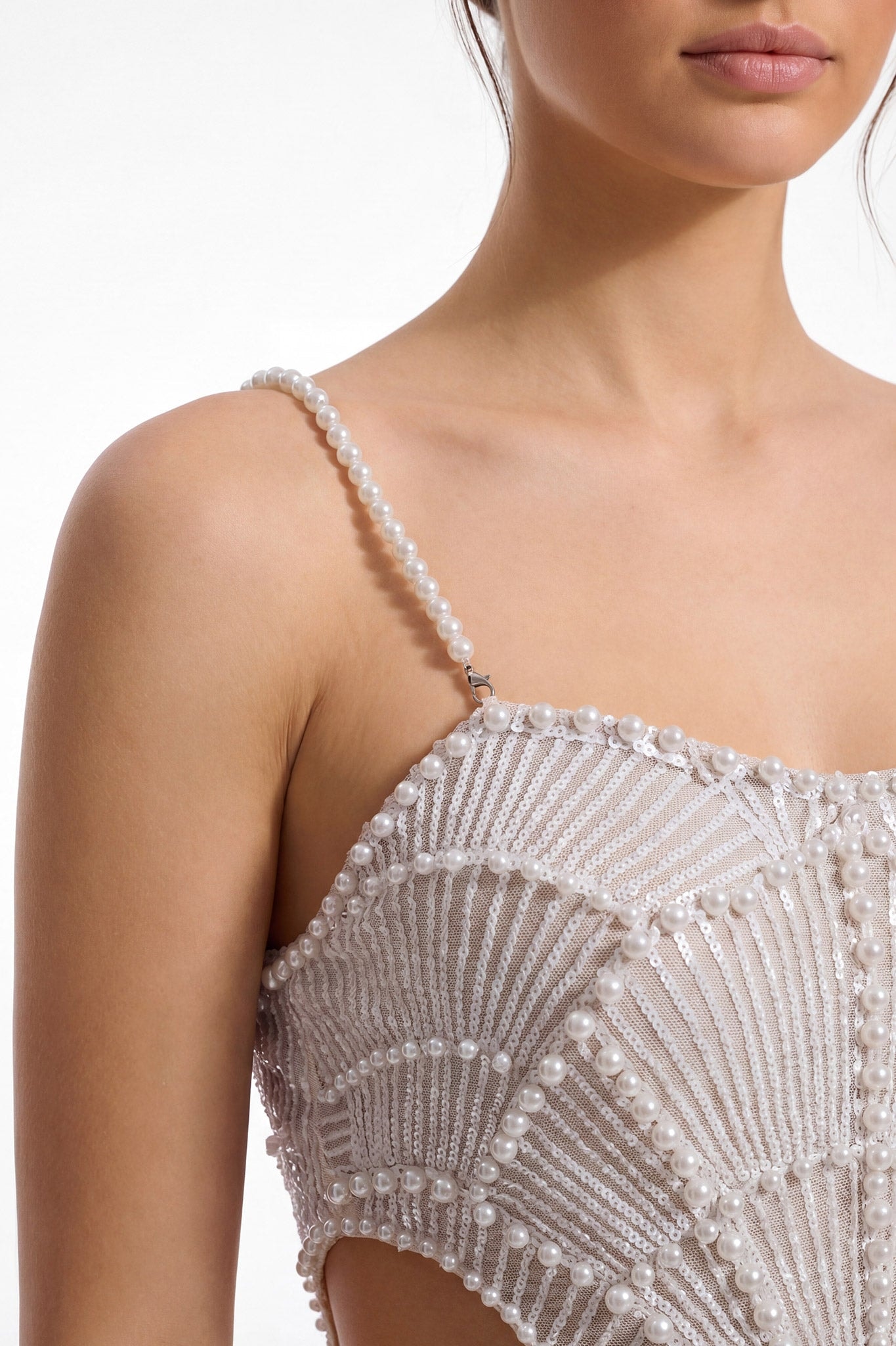 Close-up detail of white midi evening dress worn, strap and bust with pearls and champagne sequins