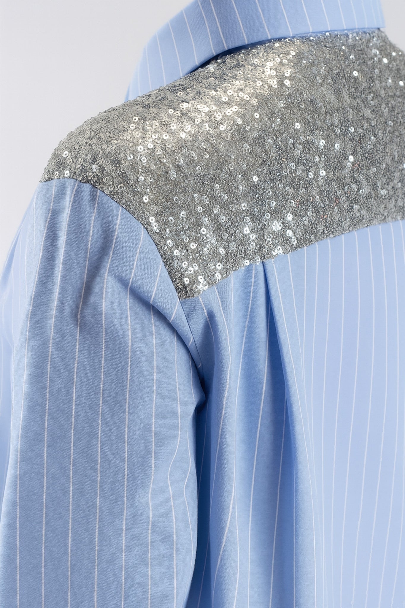Dettagli scintillanti sulle spalle di una camicia a righe azzurro cielo, che aggiungono un tocco chic per un'occasione speciale.