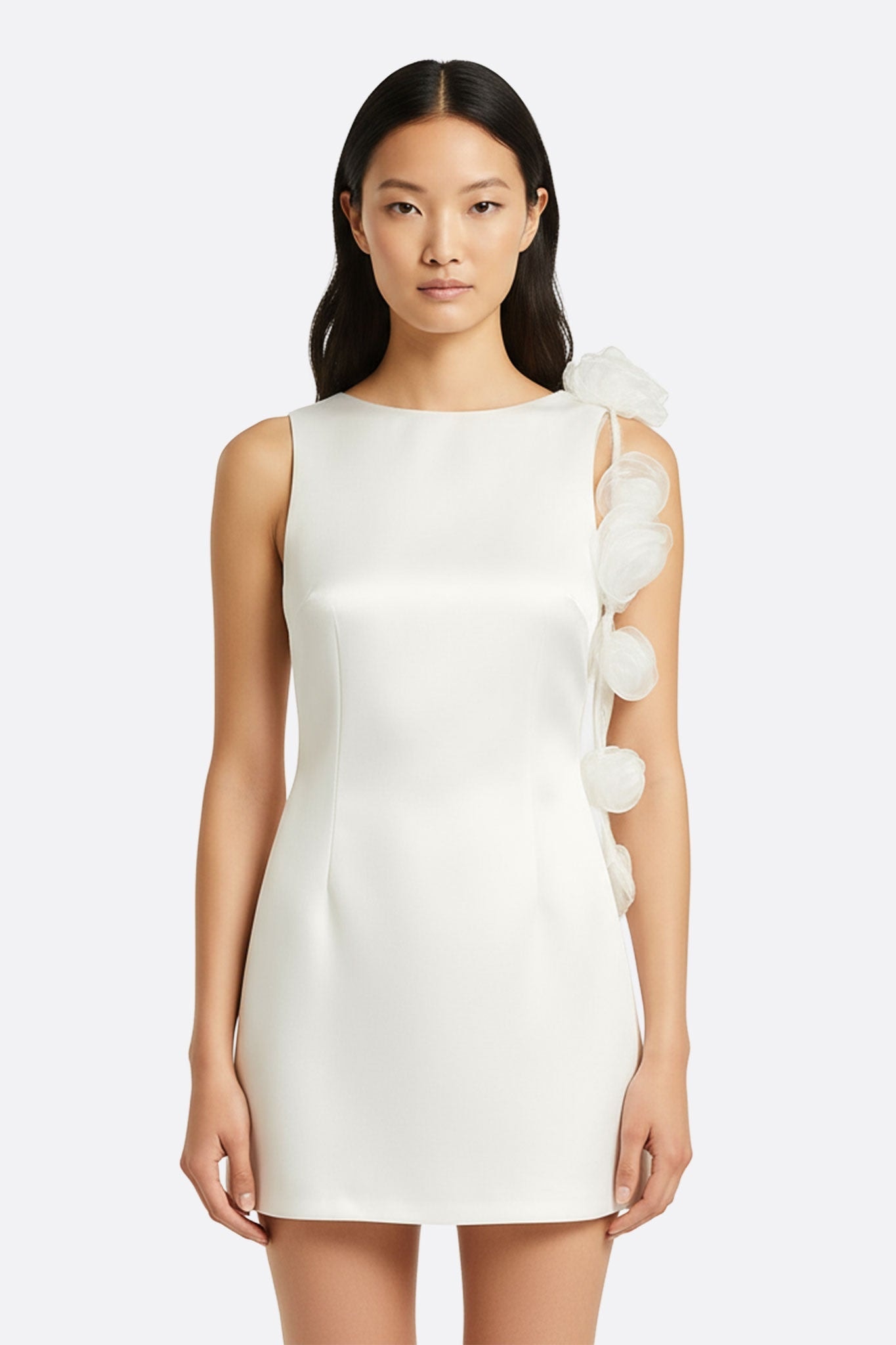 Détail de la robe blanche satinée, mettant en valeur le dos nu et les fleurs sculpturales, parfait pour une soirée chic.