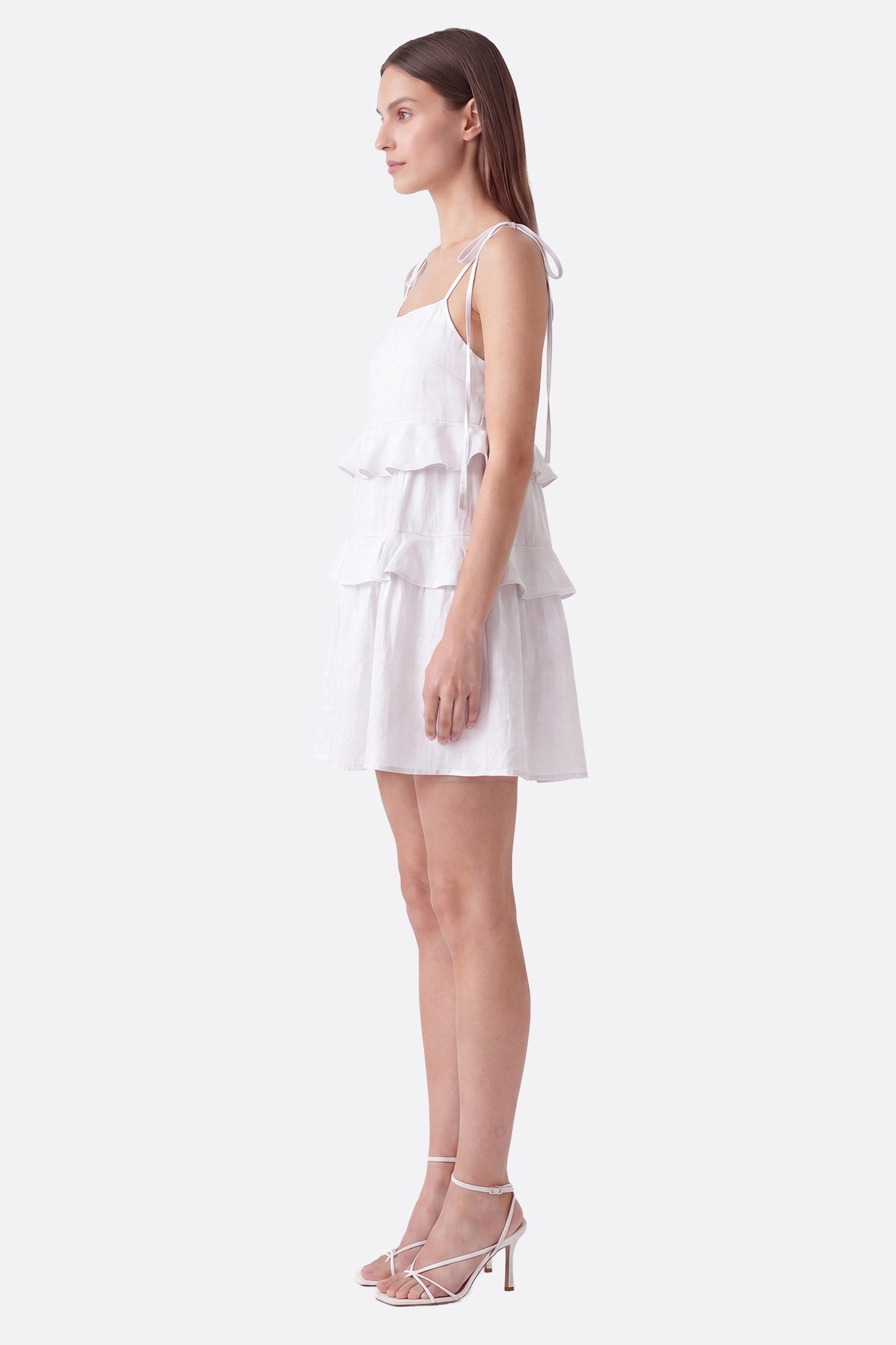 Vestido corto blanco con volantes y tirantes anudados llevado de perfil sobre maniquí, detalle de textura de lino