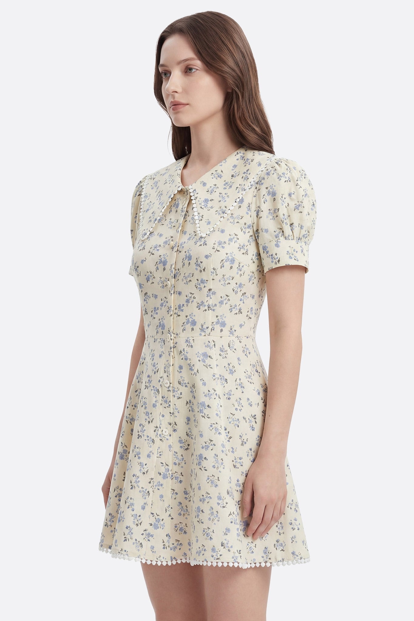 Modelo de perfil con vestido corto floral de algodón beige, cuello claudine y borde de pompones