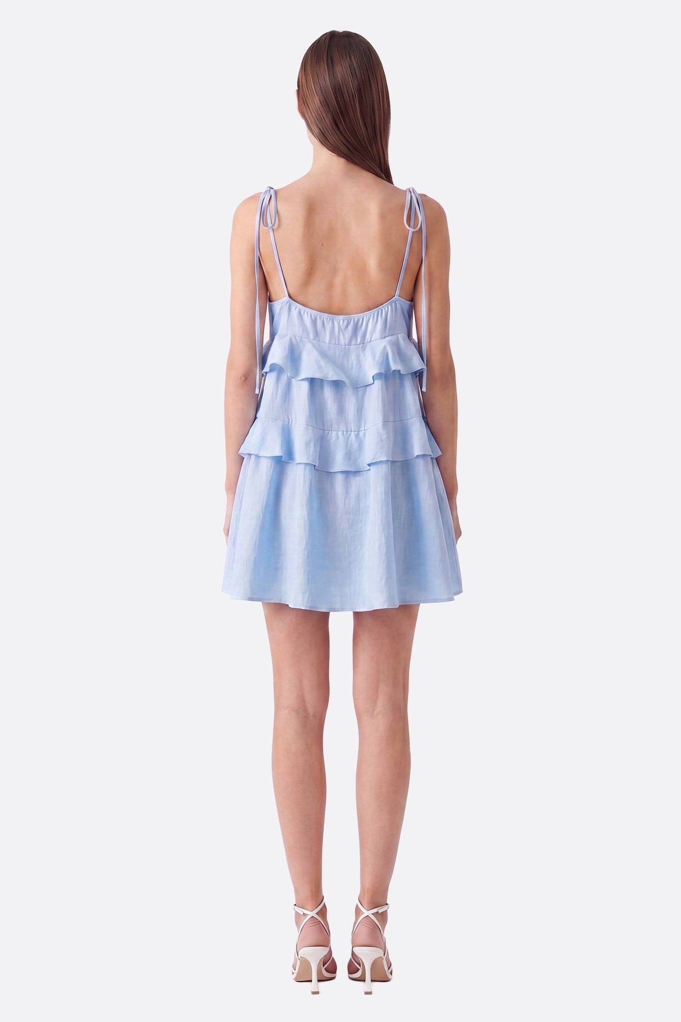 Model von hinten in einem hellblauen kurzen Kleid mit Volants und gebundenen Trägern