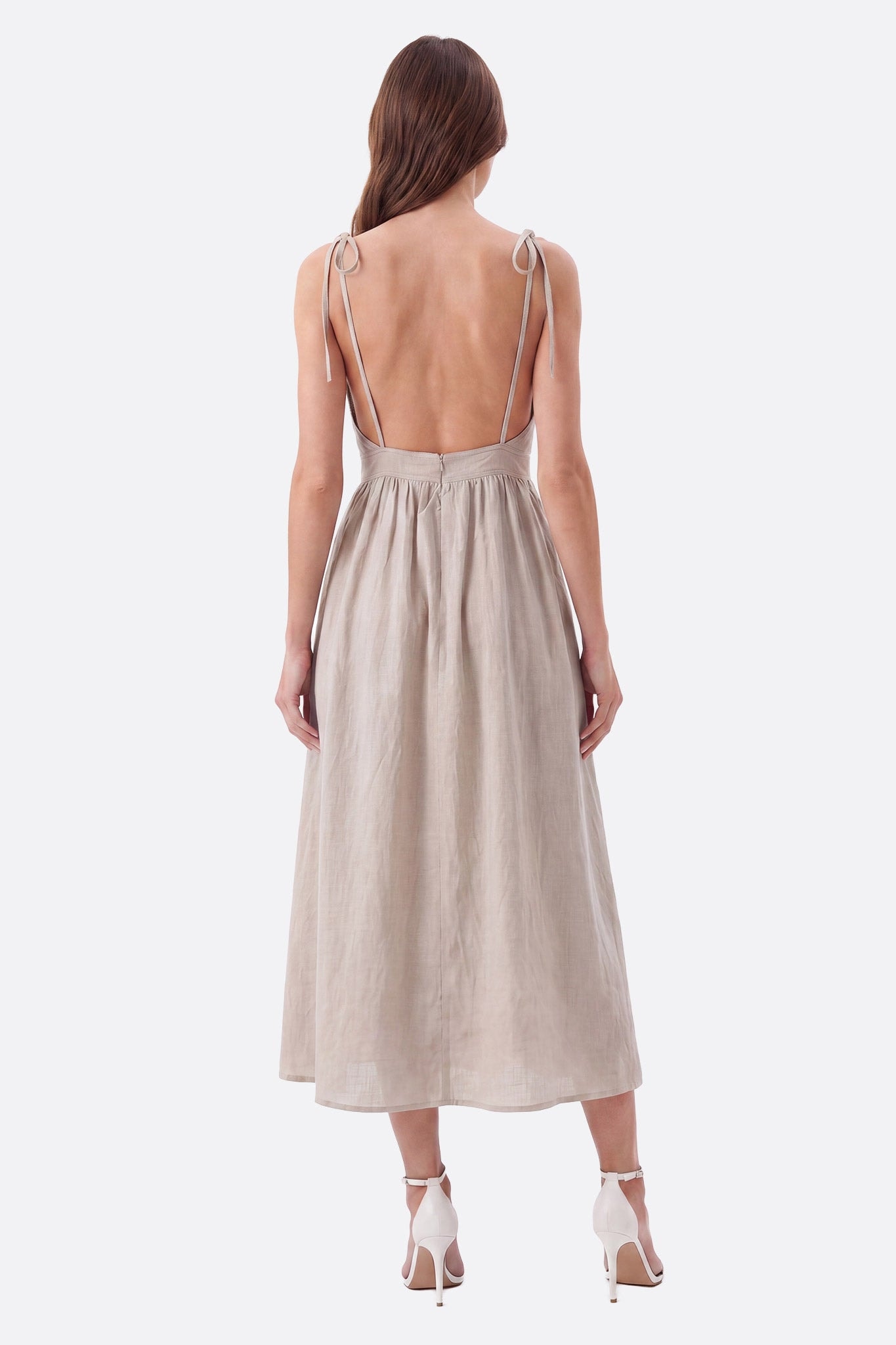 Robe midi beige portée de dos, dos ouvert et bretelles fines nouées sur les épaules