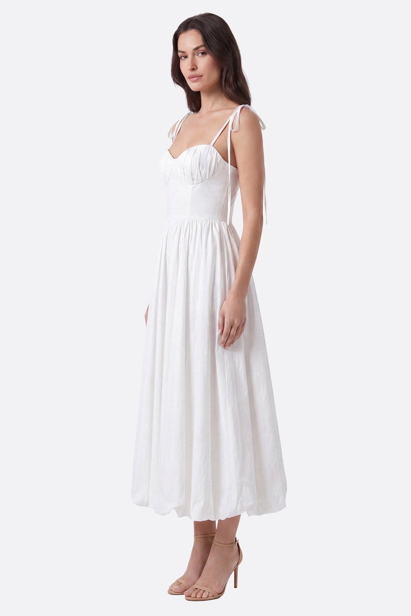 Mannequin de profil portant une robe midi blanche à bretelles nouées, bustier froncé et jupe ample