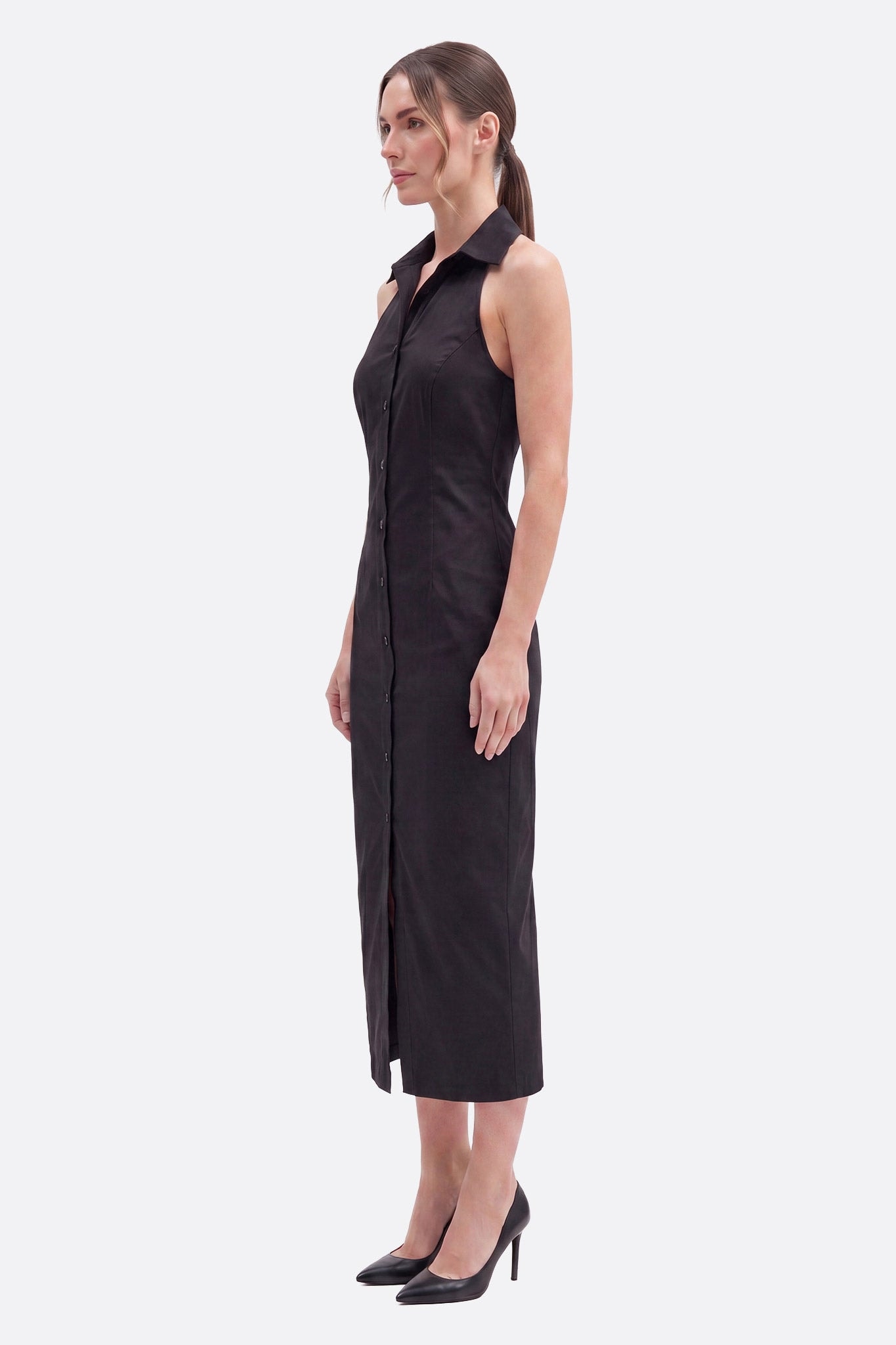Model im Profil in schwarzem Midikleid mit Hemdkragen und durchgehender Knopfleiste, vorderer Schlitz