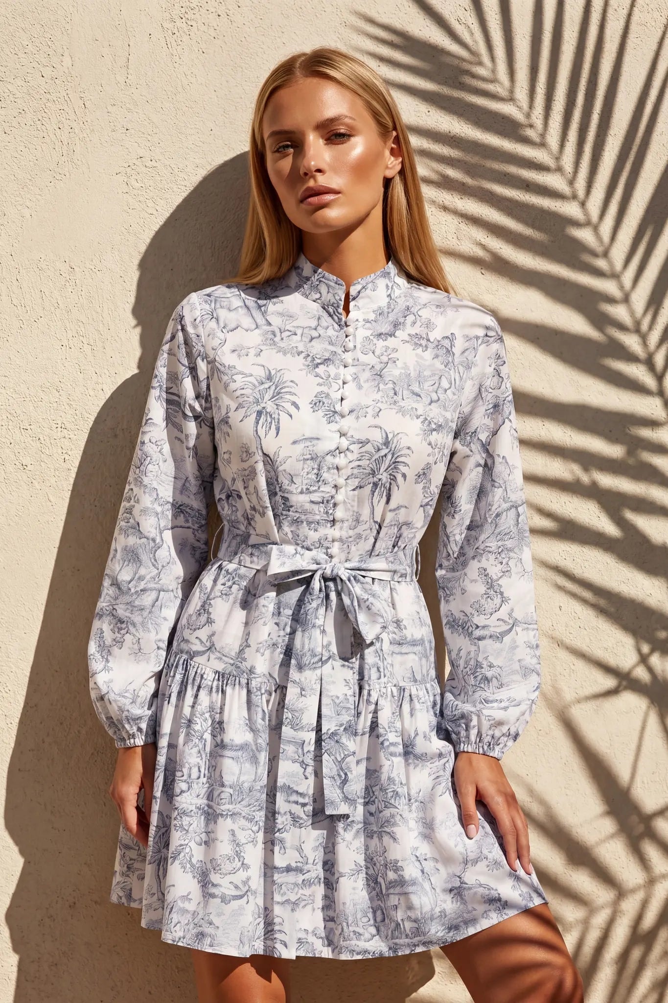 Blondes frontales Model in einem kurzen Toile-de-Jouy-Kleid mit Taillengürtel, Stehkragen und Knöpfen