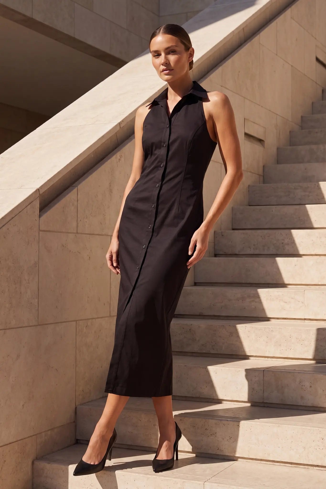 Model frontal in schwarzem Midikleid mit Hemdkragen, vorne geknöpft, auf Treppenstufen
