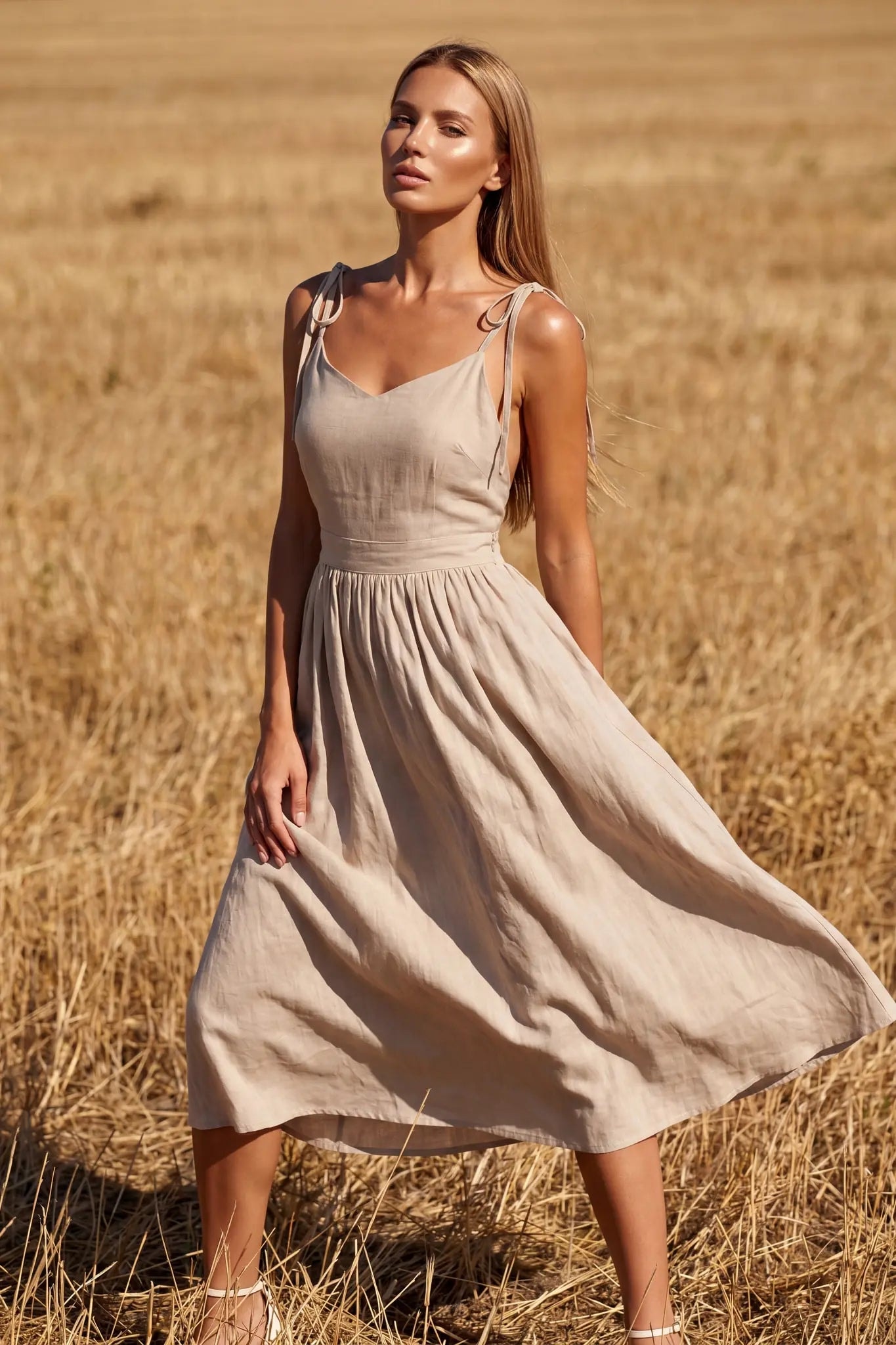 Robe midi beige à dos ouvert et bretelles nouées portée de face dans un champ de blé