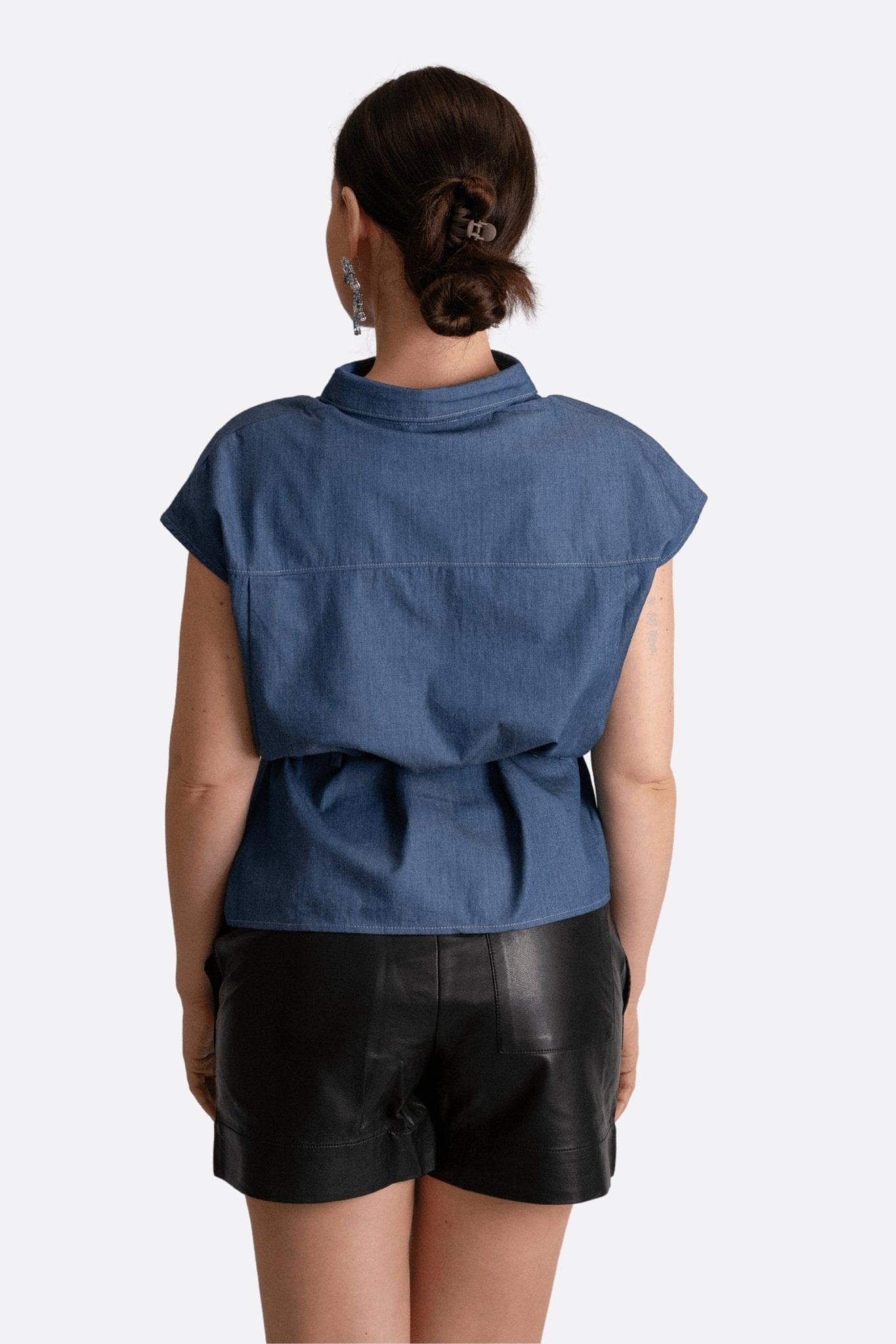 Elegant detail of the sleeveless blue denim blouse, featuring a classic collar and a refined patch pocket.