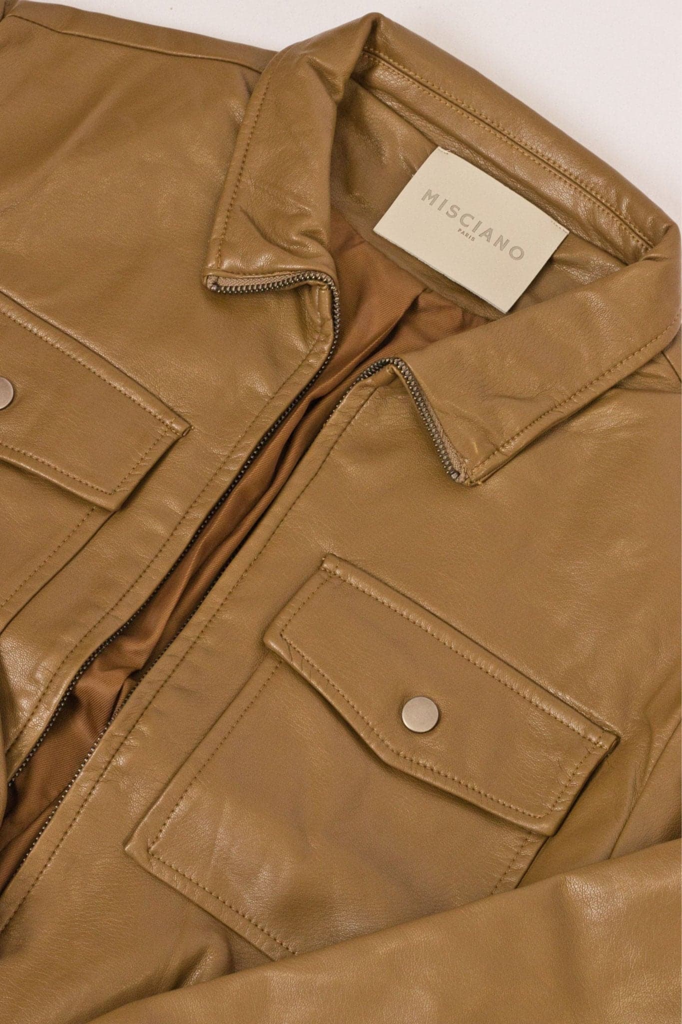 Primo piano sul giubbotto in similpelle caramello, che rivela la texture sottile e le cuciture precise per uno stile elegante.