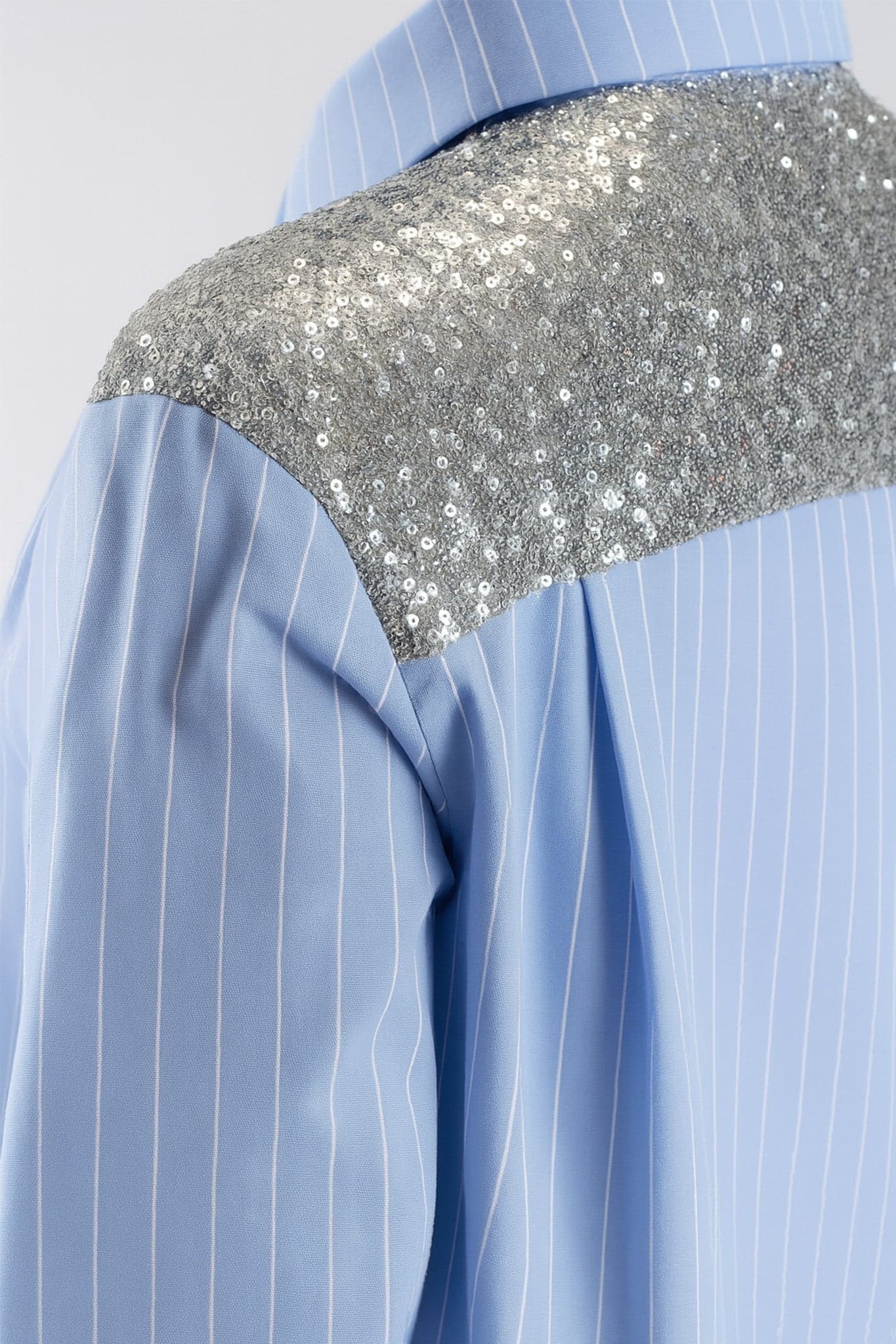 Shimmering details on the shoulders of a sky blue striped shirt, adding a chic touch for a special occasion.