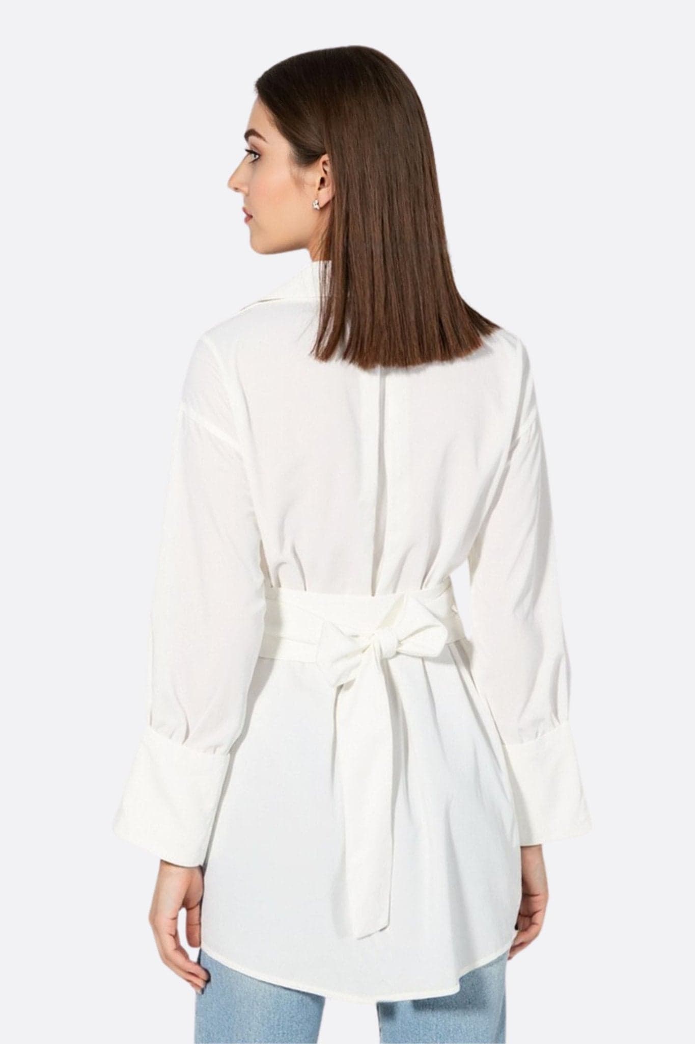 Detail des weißen fließenden Hemds mit drapiertem Gürtel, hebt den asymmetrischen Schnitt hervor, perfekt für einen eleganten Abend.