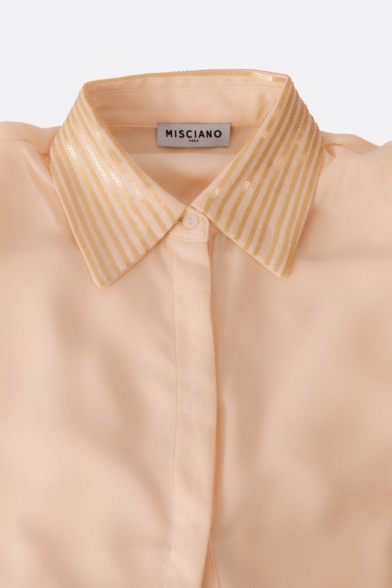 Dettaglio raffinato della schiena di una camicia rosa dal colletto classico, ornata di paillettes per uno stile chic e luminoso.