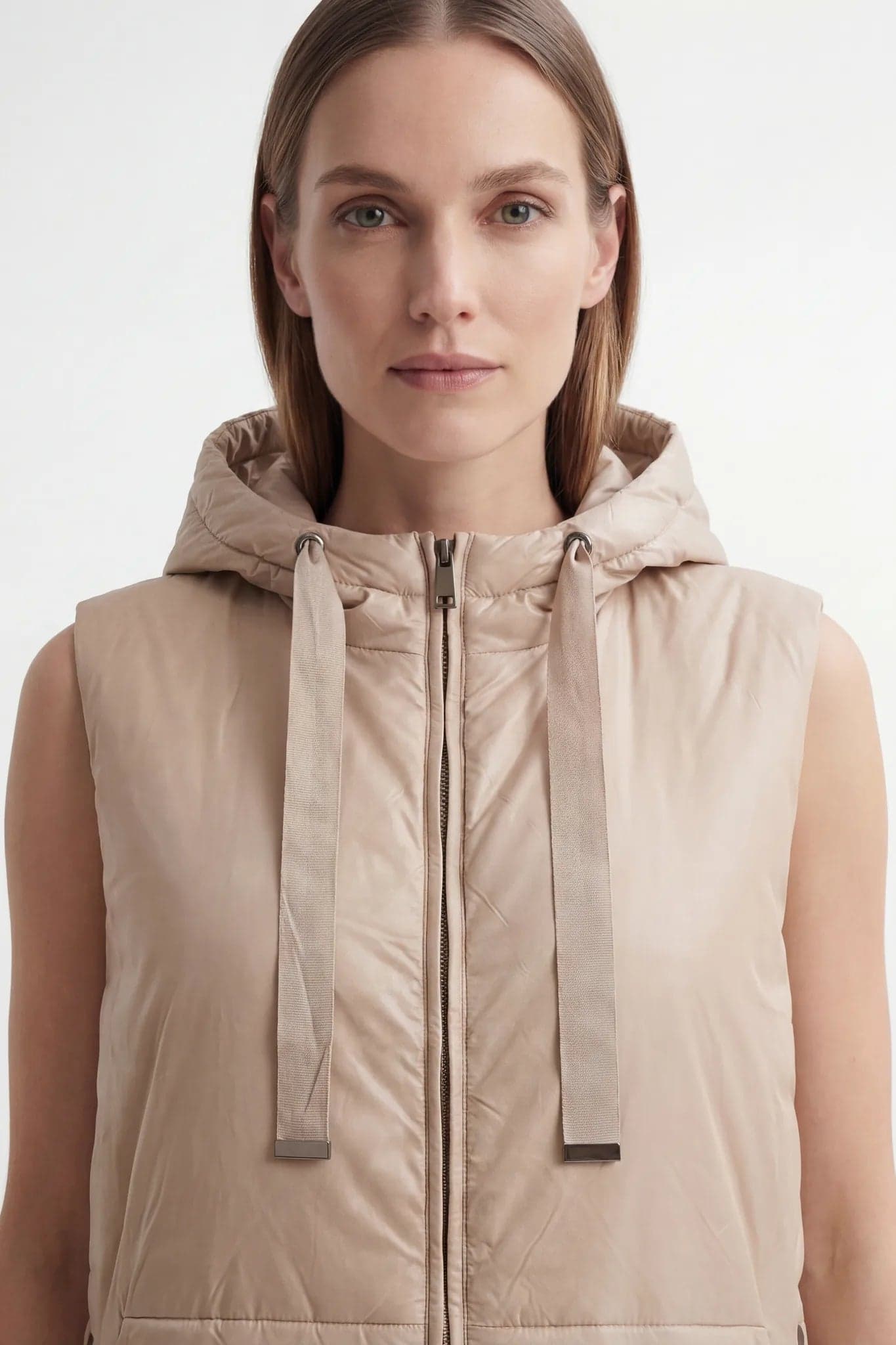 Long beige sleeveless down coat with hood, highlighting the seams and fabric, ideal for a refined winter look.