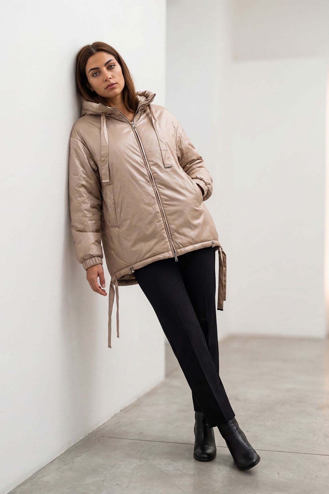 Piumino beige satinato con cappuccio, dettaglio dei lacci regolabili e della texture trapuntata, ideale per un'uscita...