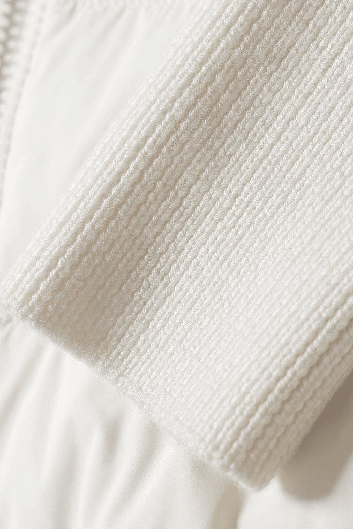 Detail der Kapuze der weißen zweimaterialigen Daunenjacke mit Entendaunen, Symbol für Komfort für einen schicken und eleganten Winter.
