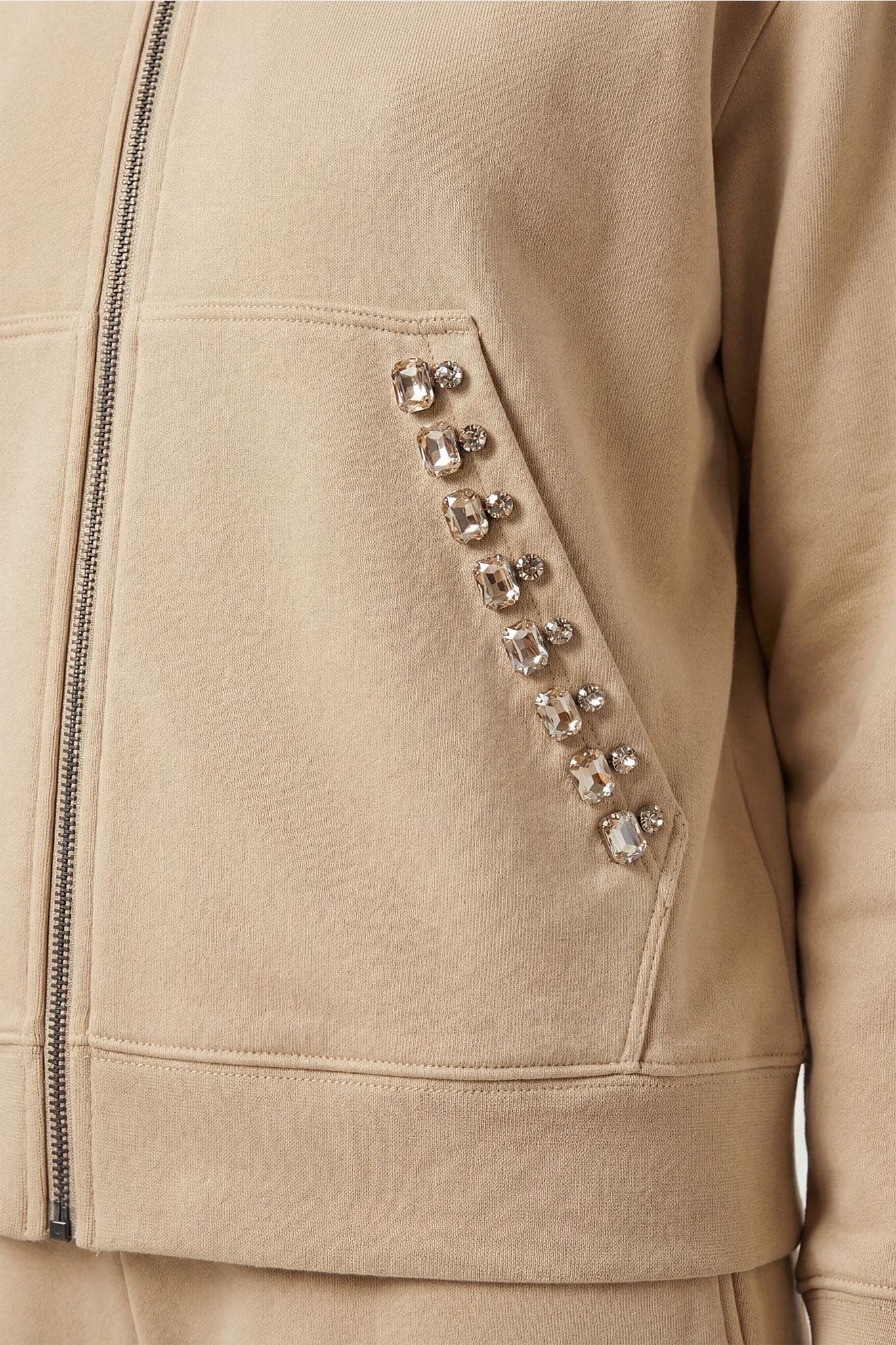 Détail d'un ensemble de survêtement beige avec cristaux, alliant confort et élégance pour les occasions spéciales.