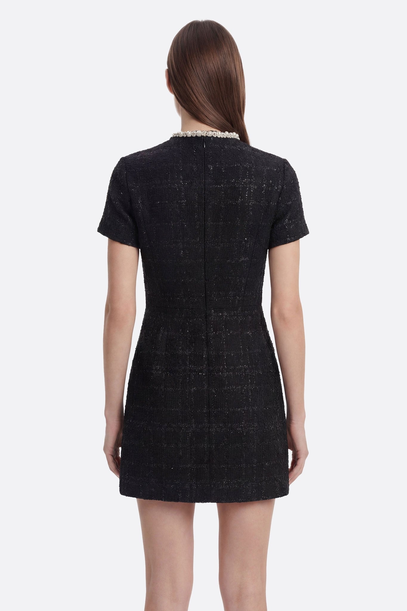 Vestido corto negro de tweed con cristales y perlas, ángulo diferente que resalta su elegancia atemporal.