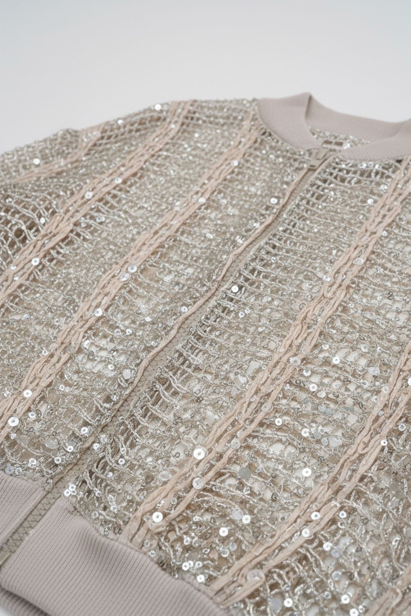 Detail of the champagne openwork bomber vest in linen and silk, revealing sparkling sequins for a refined look and...