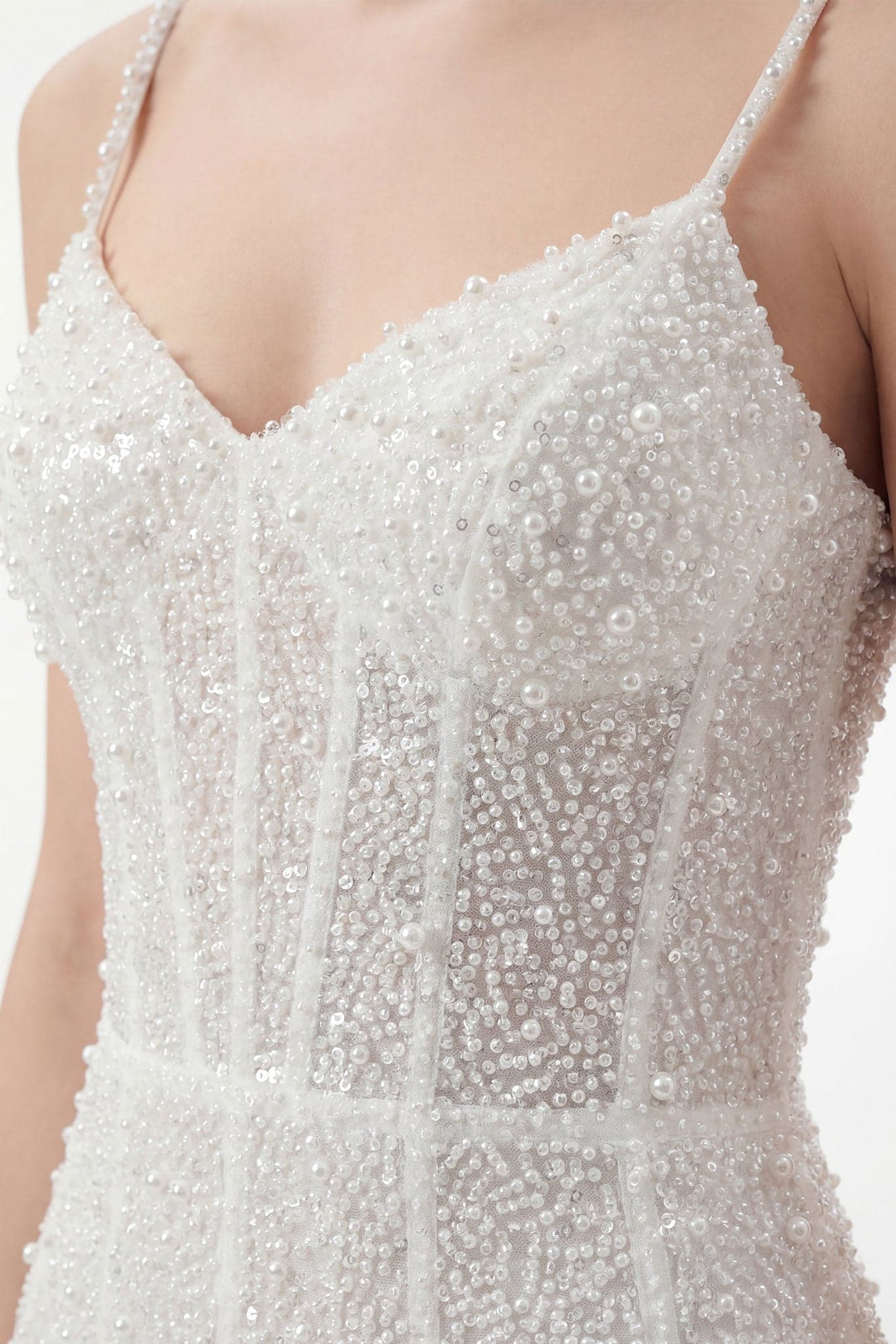 Detail der Träger eines weißen kurzen Kleides, verziert mit Perlen, ideal für eine elegante Veranstaltung oder ein raffinierte Abendessen.