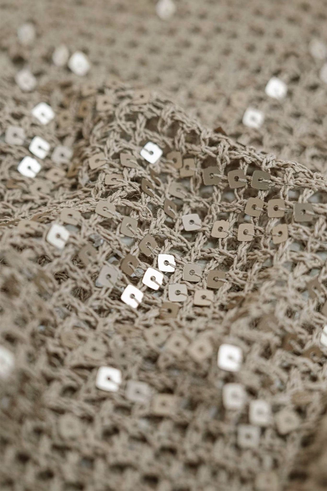 Elegant detail of a sand beige openwork knit polo, enriched with tone-on-tone sequins, ideal for a chic summer outfit.