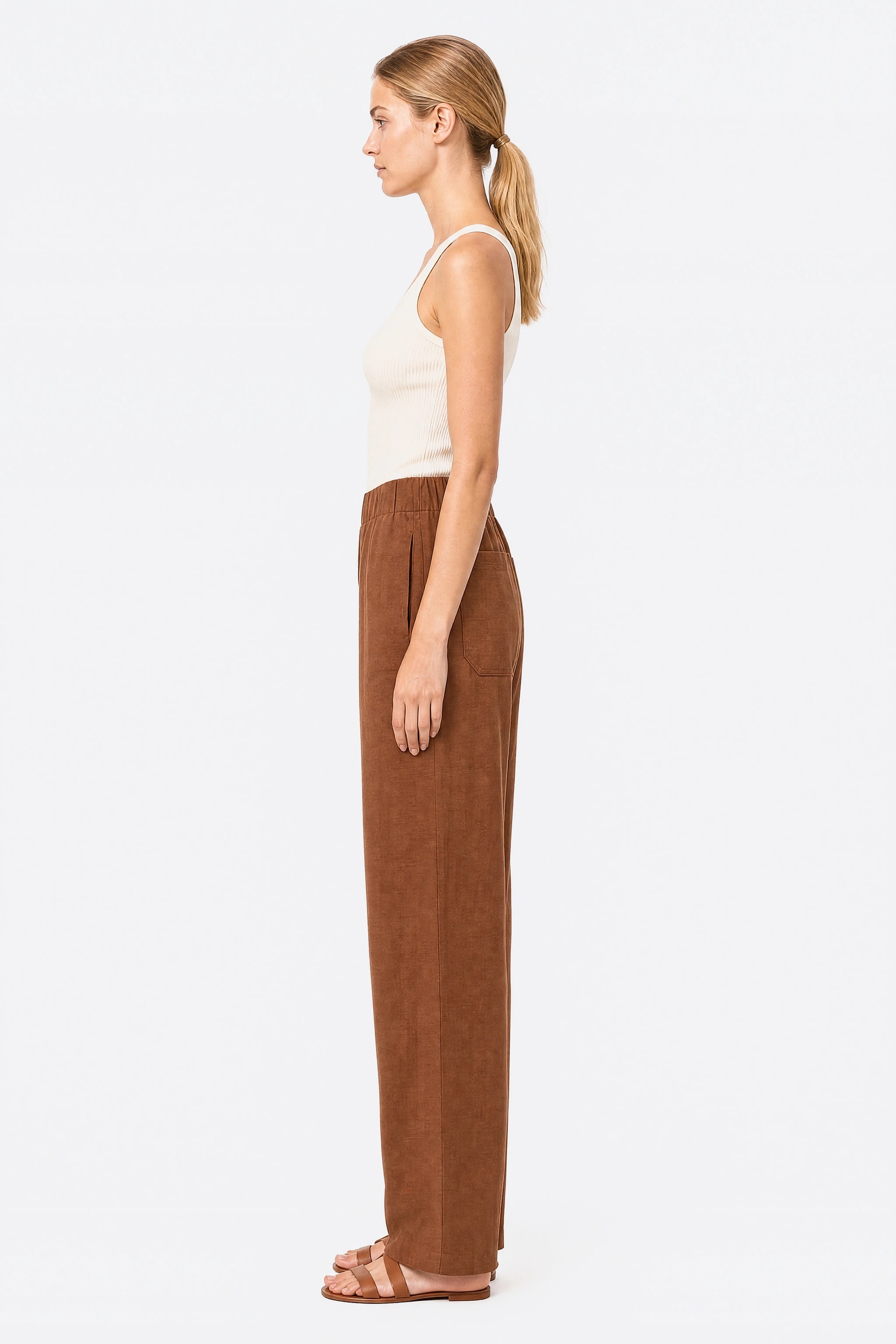 Profile of the wide brown linen pants showing the side-seam pocket and the wide straight leg falling to the ankle