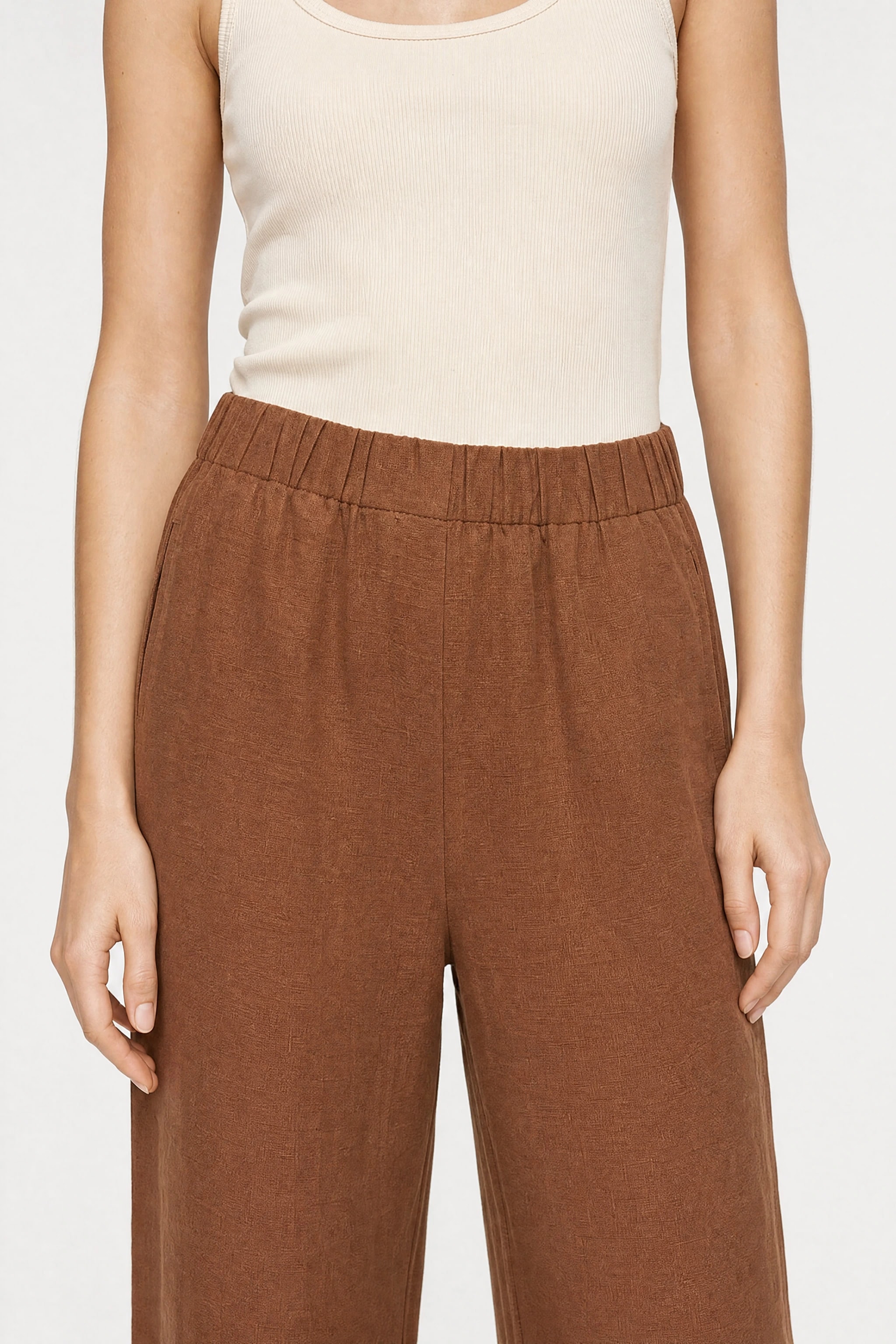 Wide brown linen pants worn, close-up view from bust to knees with the cream tank top tucked in and the flat front