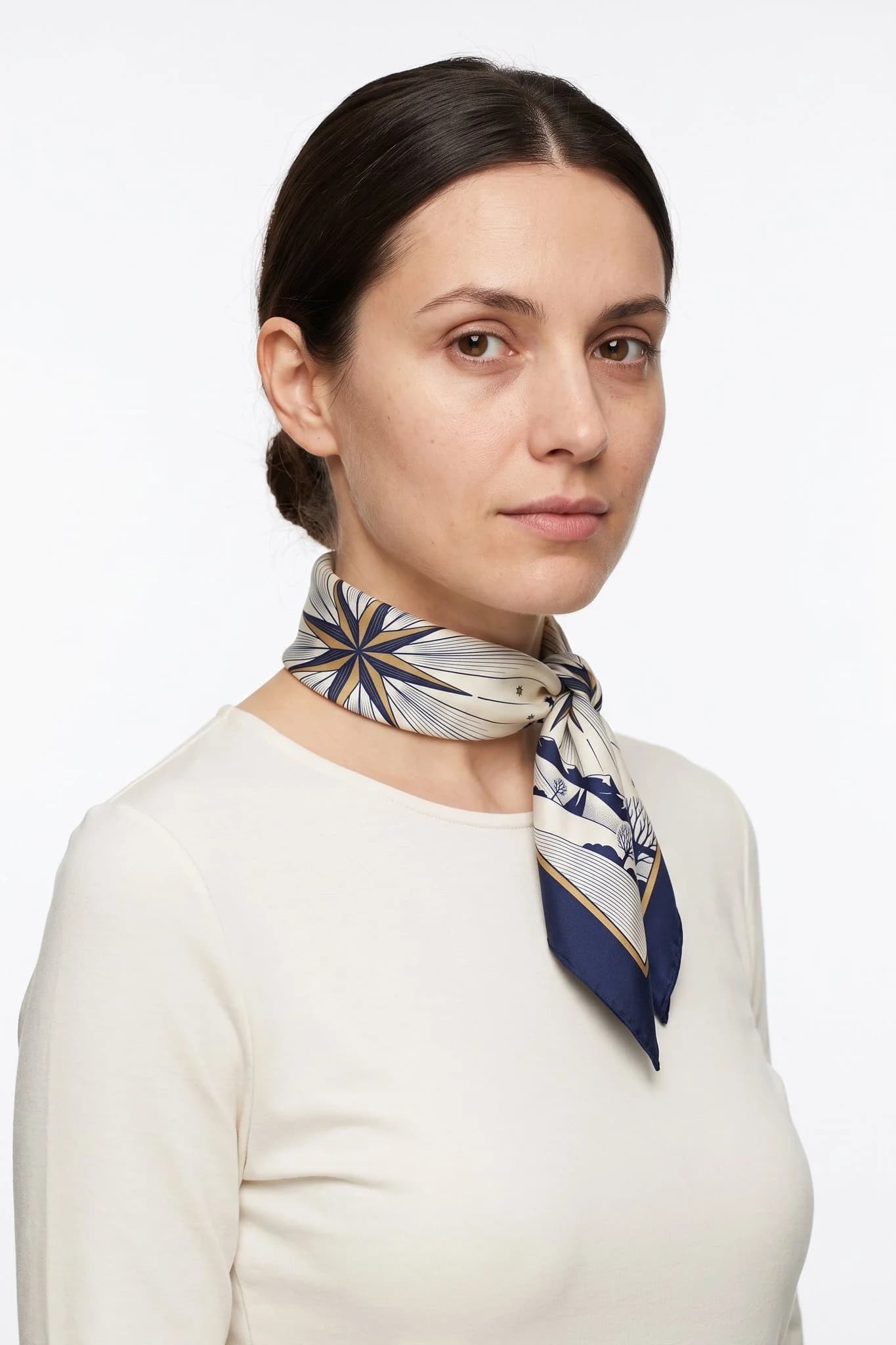 Fazzoletto piccolo di seta 50 Étoile du berger indossato annodato al collo come piccolo foulard da una donna, vista studio
