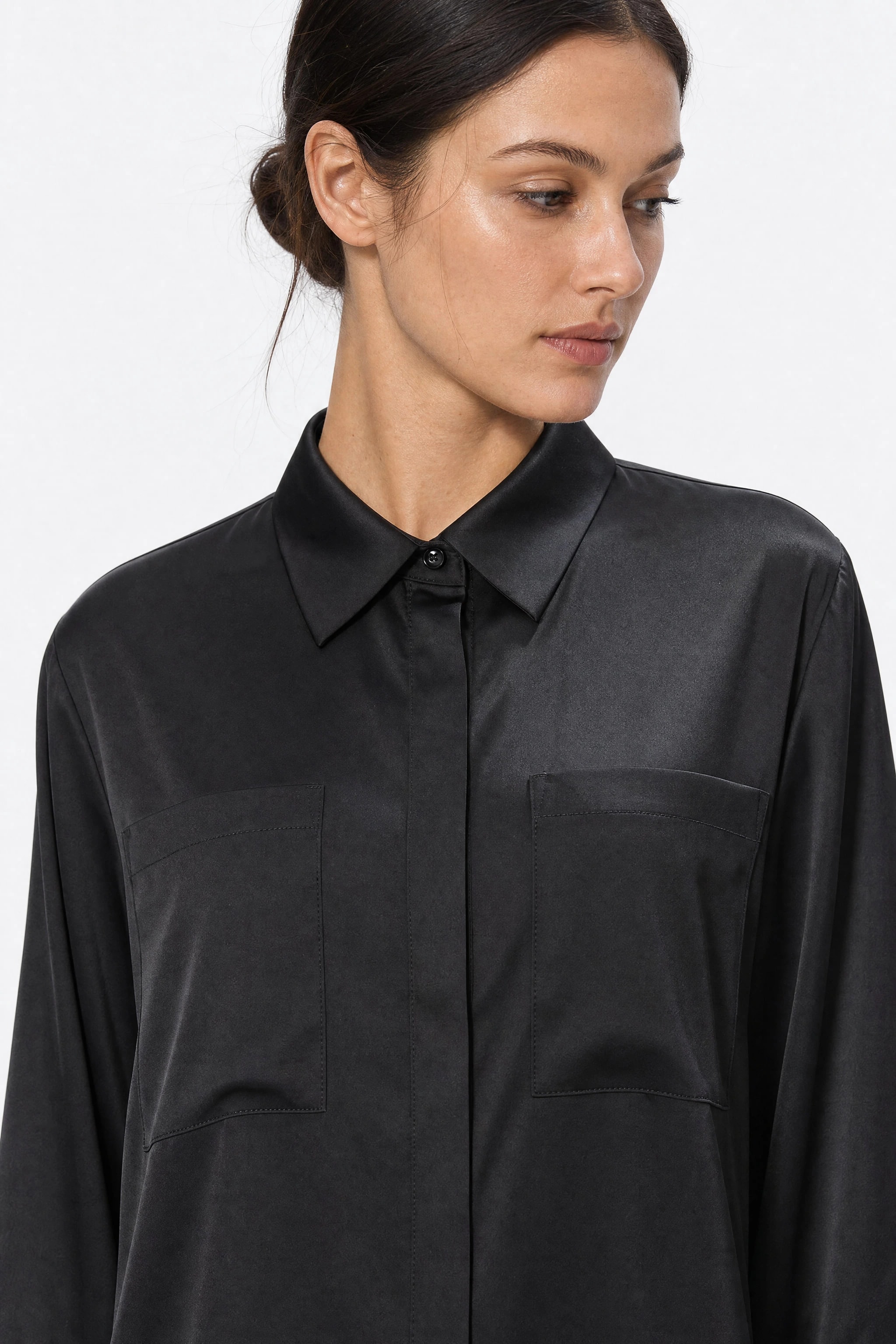 Gros plan sur le col chemise et les deux poches poitrine de la robe en satin noir