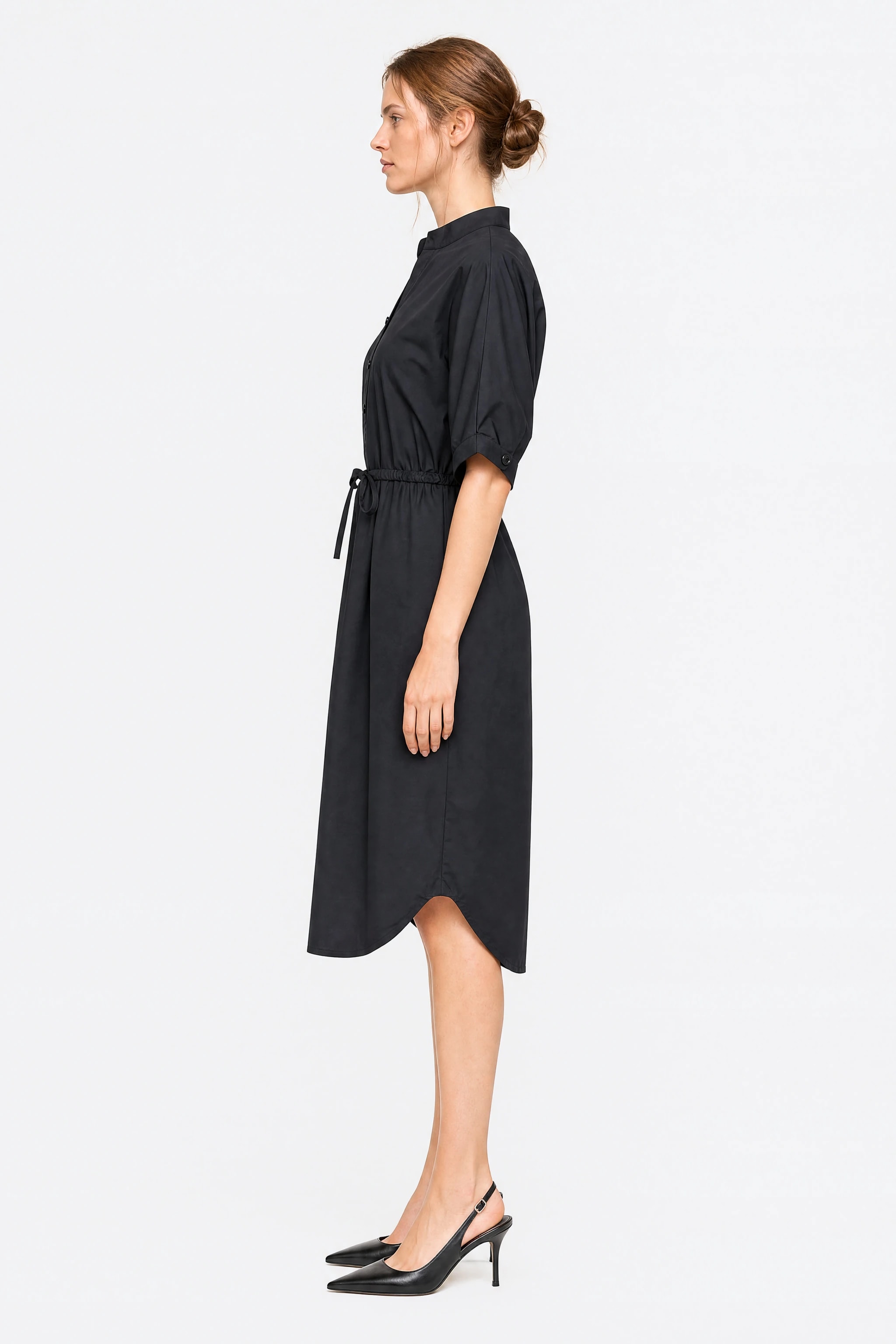 Profile of the black cotton shirt dress showing the short sleeve with turnback and flared skirt under the drawstring waist