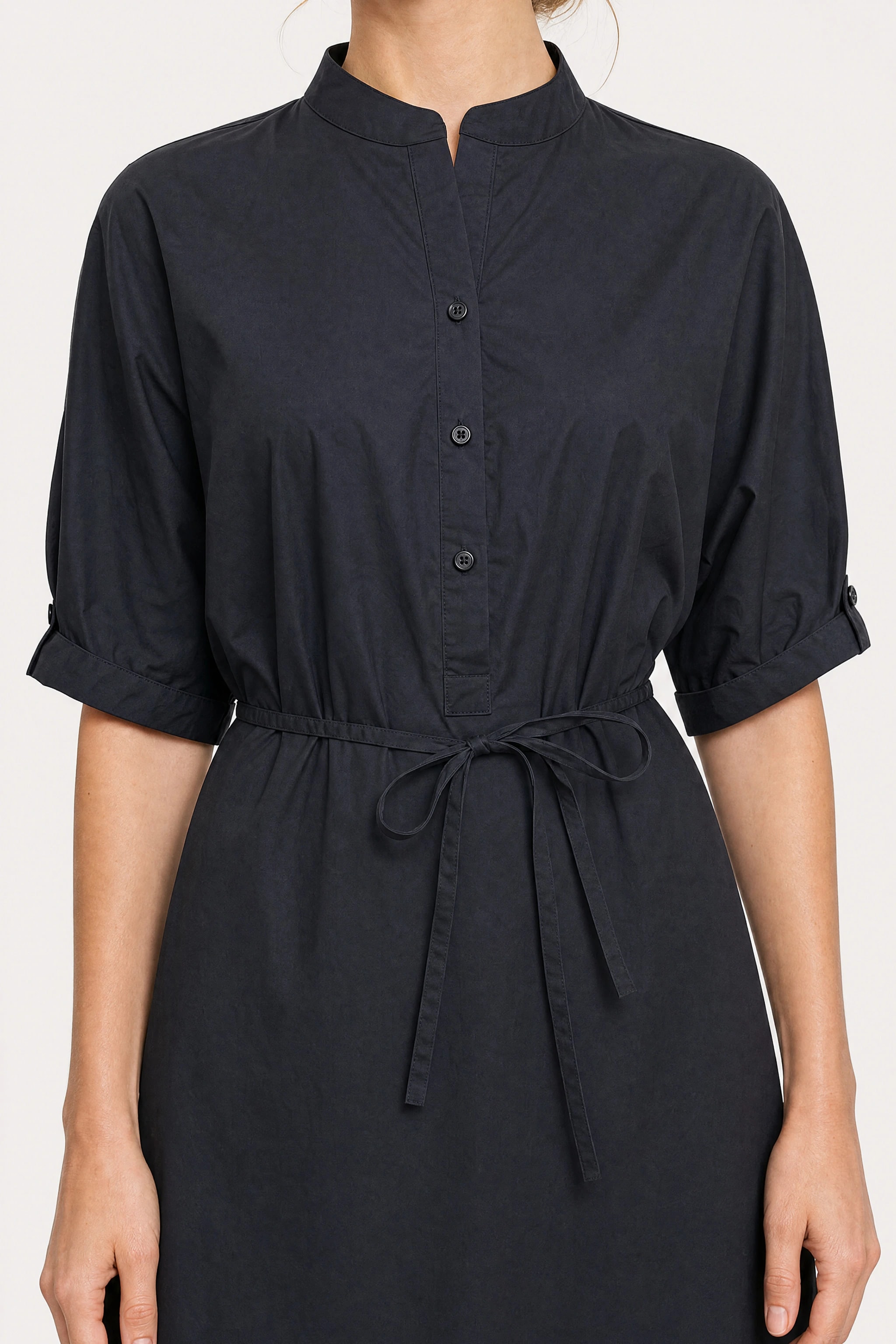 Detail of the black shirt dress: notched officer collar, half-placket buttons, tied cord and buttoned sleeve turnback