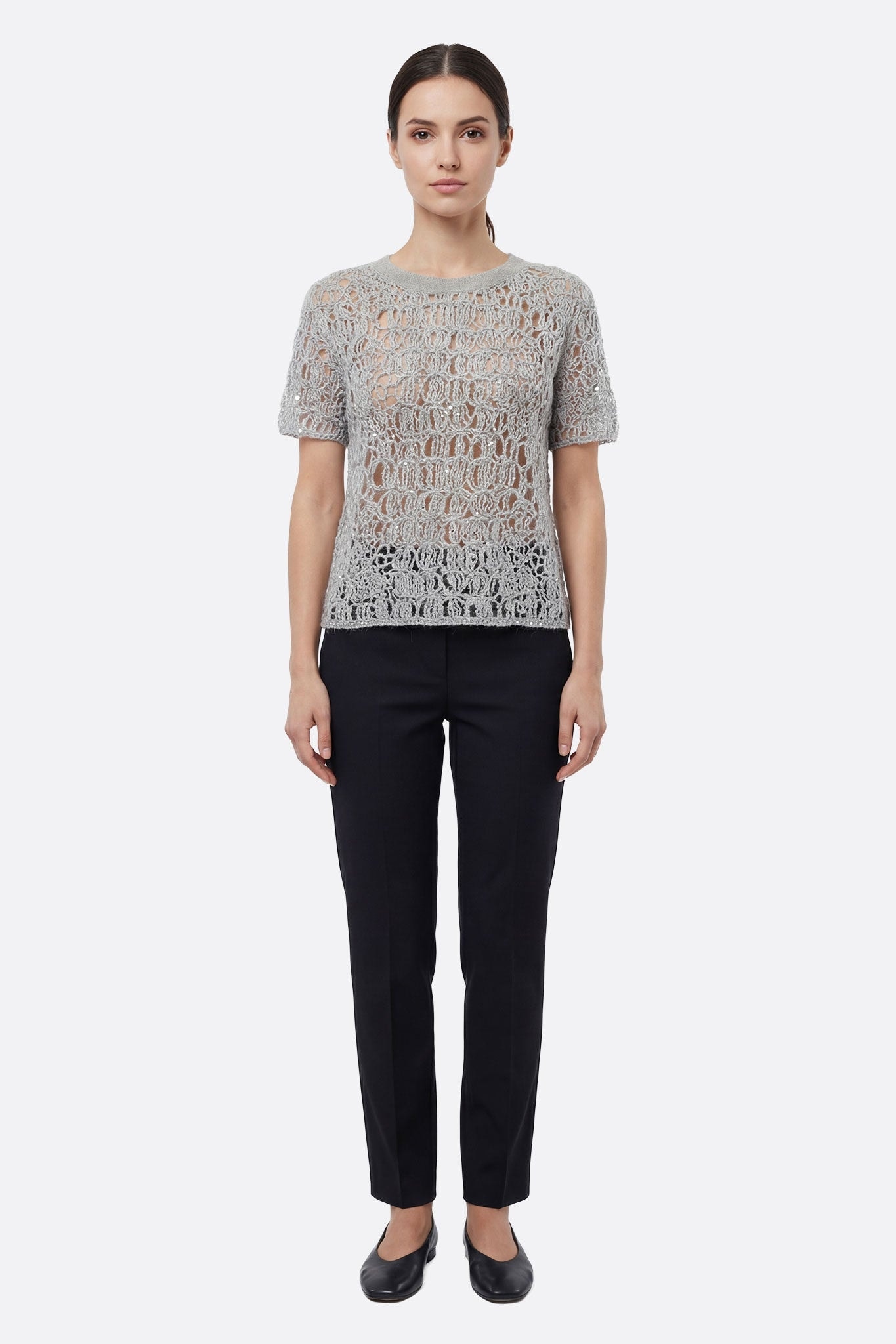 Fesselndes Detail des durchbrochenen perlgrauen Strickpullovers mit Lurex, ein elegantes Stück, um ein Sommeroutfit aufzuwerten.