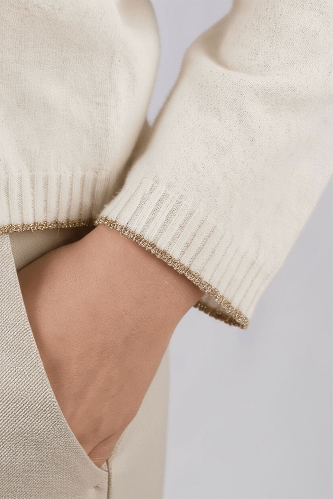 Pull beige en laine mérinos et cachemire, col V, mettant en valeur ses finitions dorées pour un style raffiné au quotidien.